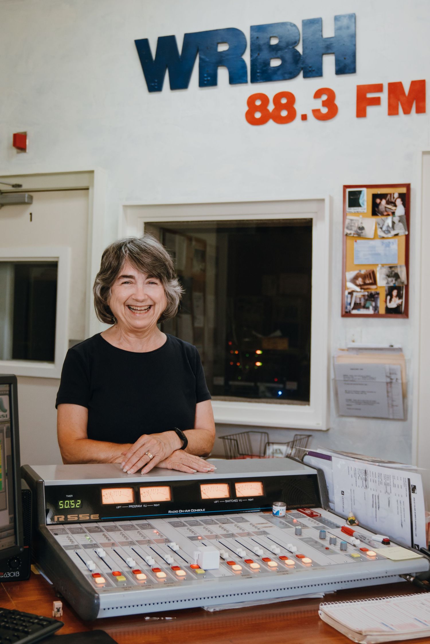 Smiling woman at WRBH 88.3 FM radio station mixing board console in a broadcast studio.