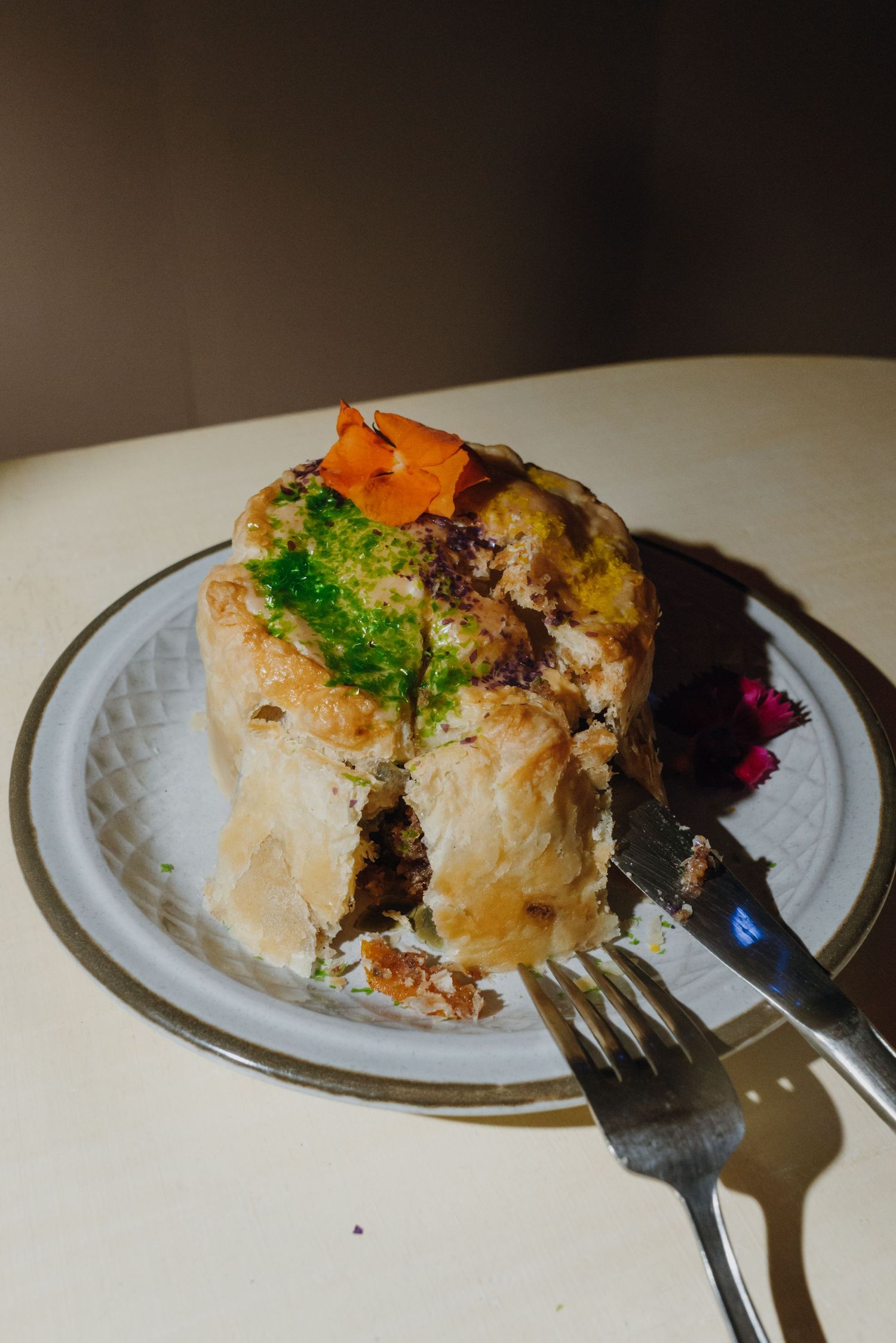 A golden pastry pie garnished with fresh herbs and carrots, served on a white plate with a fork.
