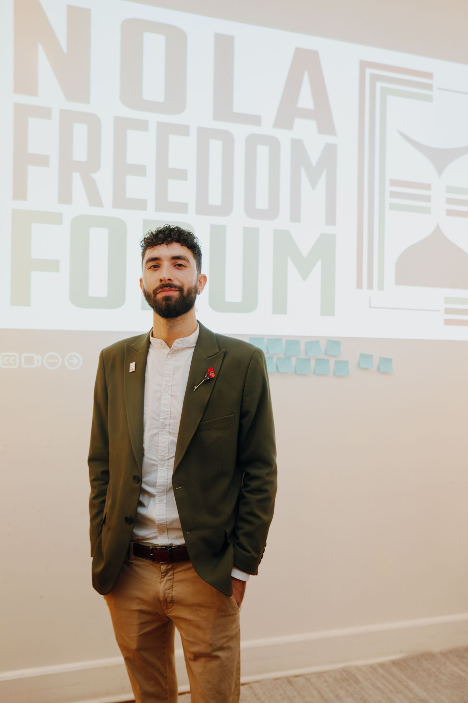 Man in olive blazer stands before NOLA Freedom Forum projected backdrop.