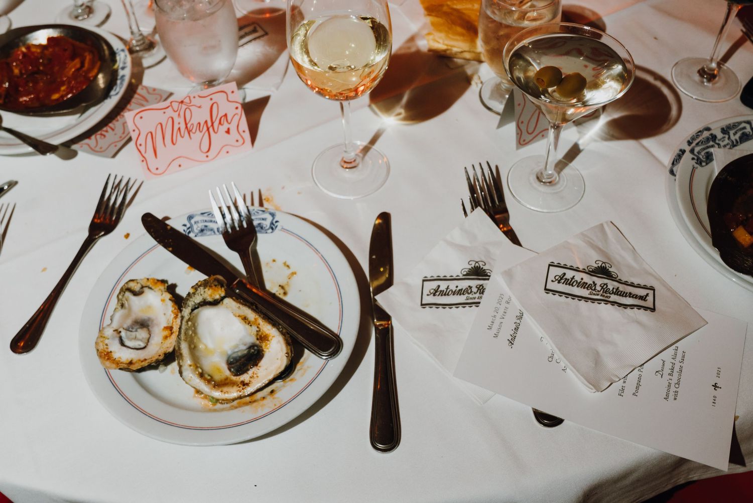 Oysters on white plate with wine glasses and place cards at elegant dinner table.
