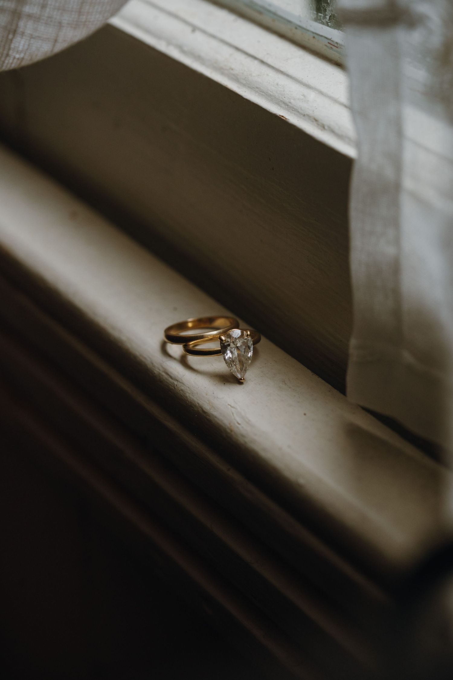 Gold wedding rings with marquise diamond displayed on a windowsill in soft natural light.