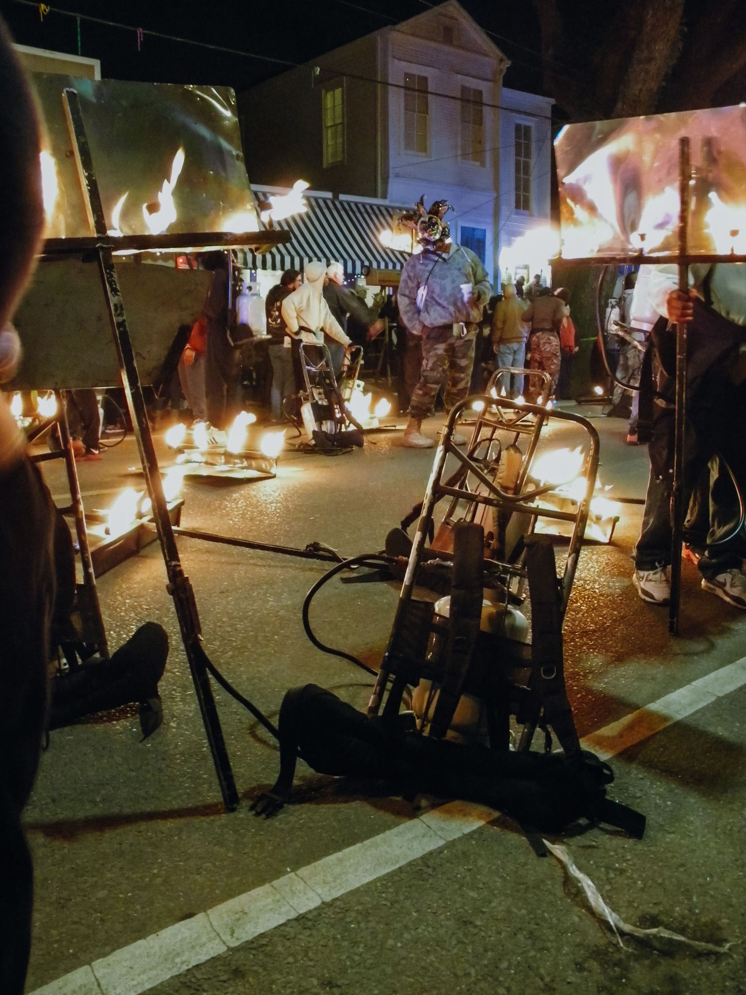 A nighttime street festival featuring fire performers with flames illuminating artwork displays and crowds.