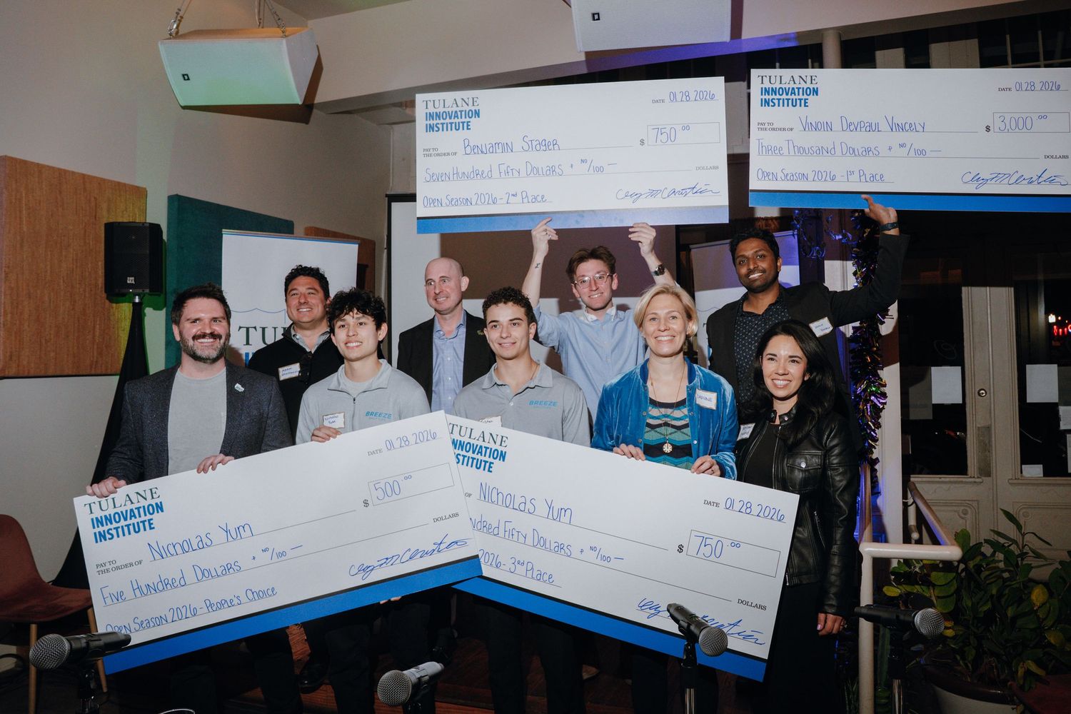 Group of winners holding large ceremonial checks at indoor innovation award ceremony.