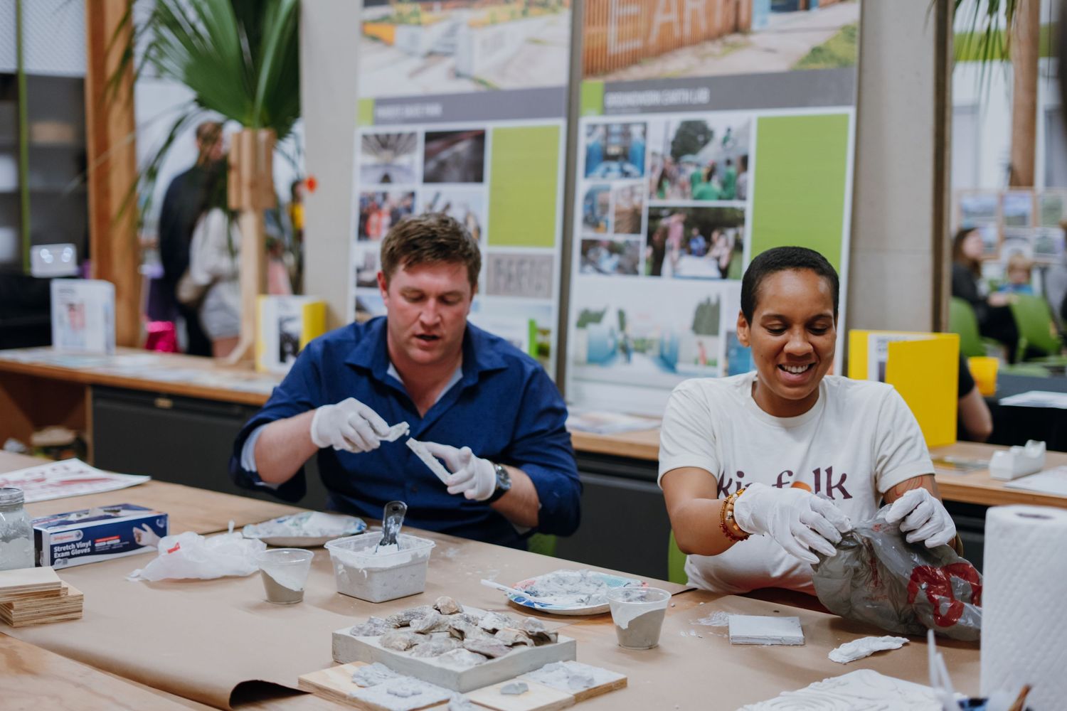 Two volunteers wearing gloves working on a crafting project at a community sustainability event.