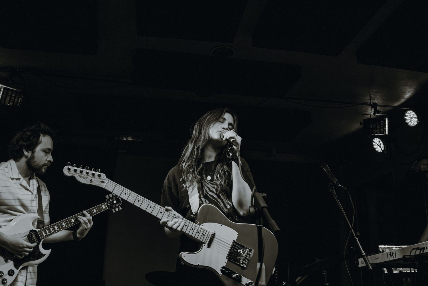 Black and white photo of female vocalist and guitarist performing live on a dimly lit stage.