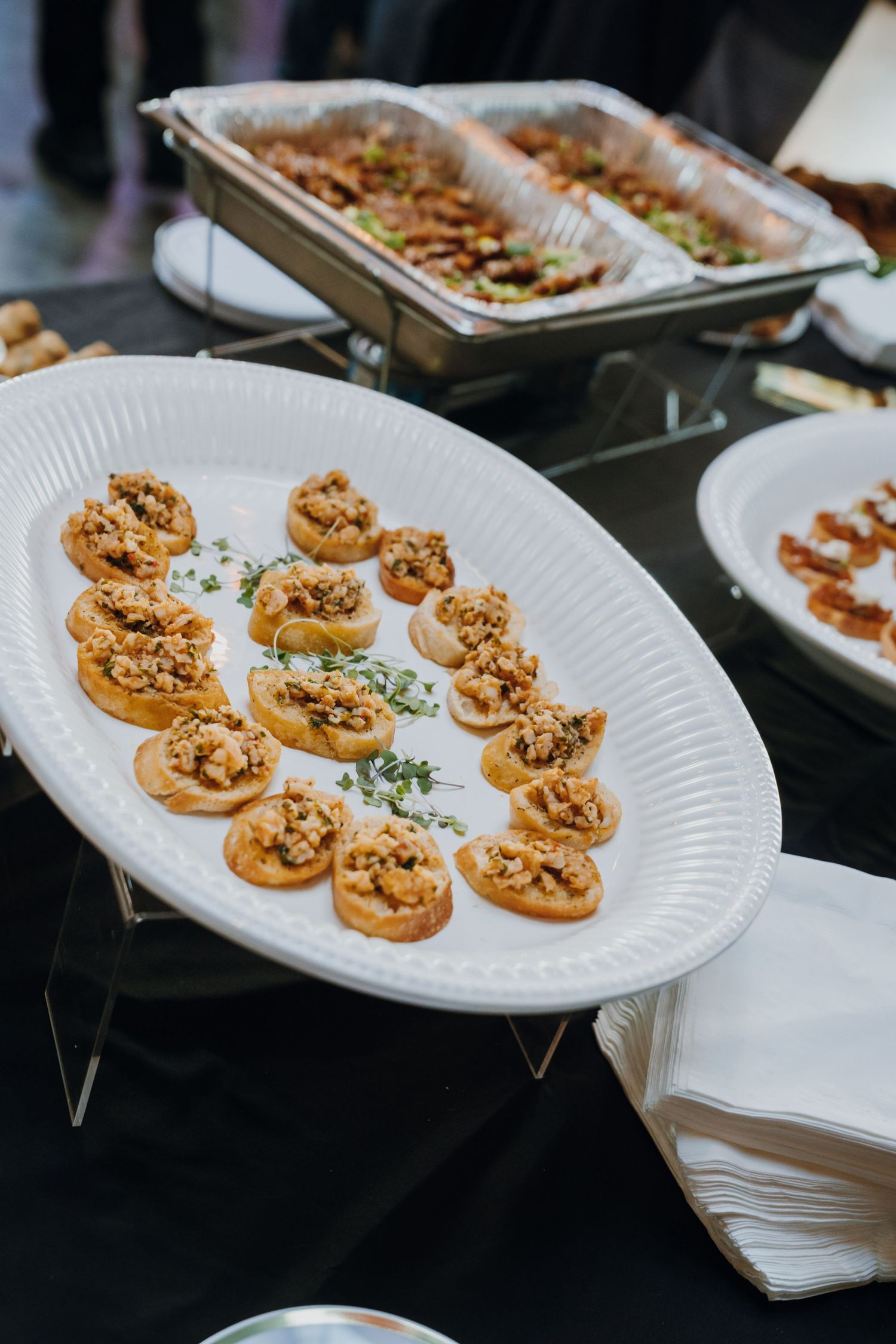 Elegant bruschetta appetizers topped with savory meat mixture arranged on a white oval serving platter.