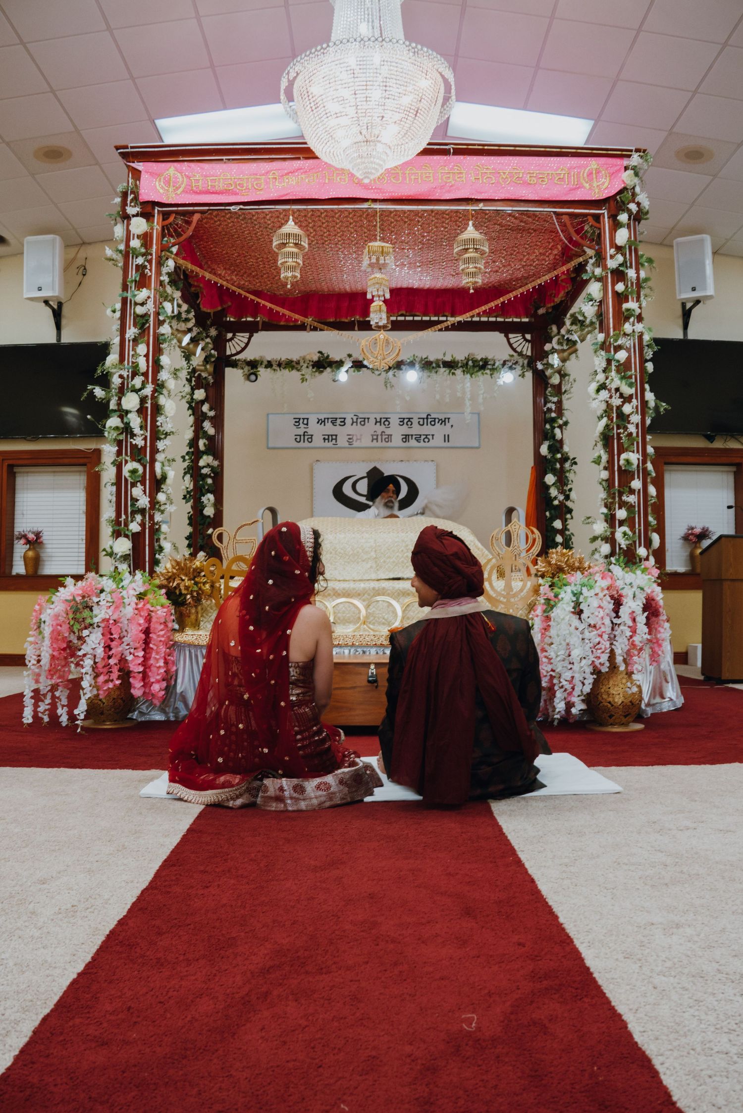 Sikh bride and groom sit before the Guru Granth Sahib at a beautifully decorated Anand Karaj ceremony.