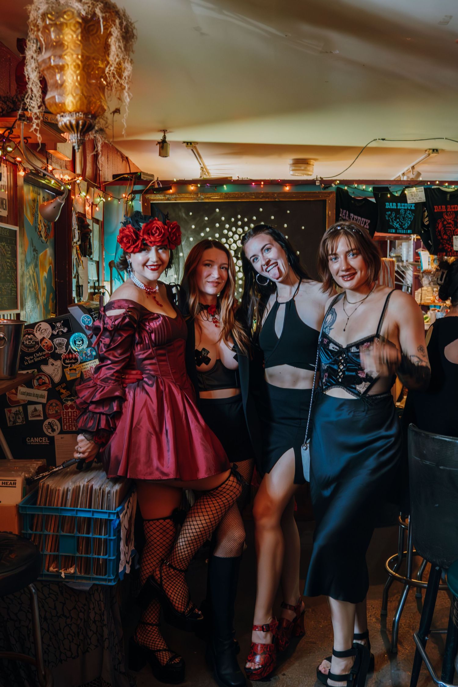 Four women in festive costumes pose together smiling inside a decorated party venue.