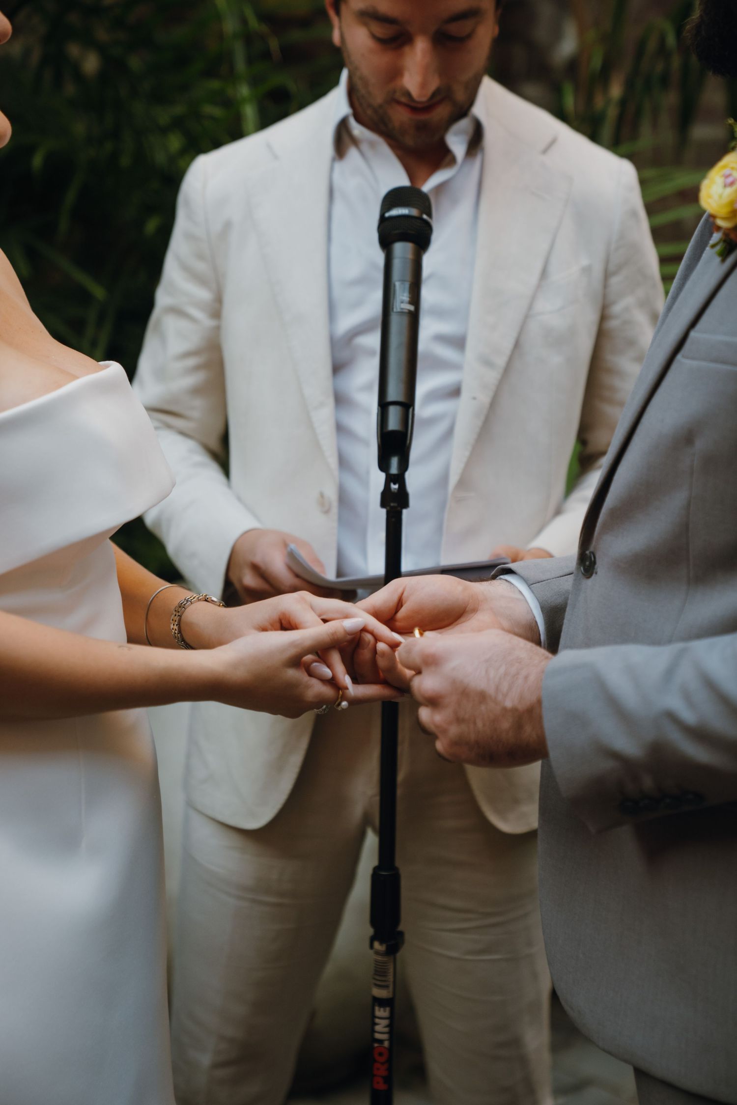 Groom places wedding ring on brides finger during outdoor ceremony as officiant in white suit looks on. New Orleans, Louisiana, Mississippi
