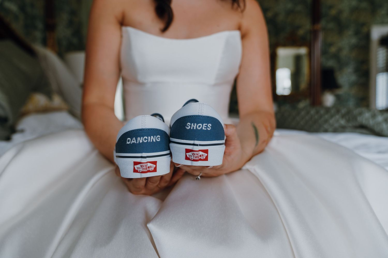 Bride in white wedding dress holding custom Vans sneakers labeled Dancing Shoes on the soles. New Orleans, Louisiana, Mississippi