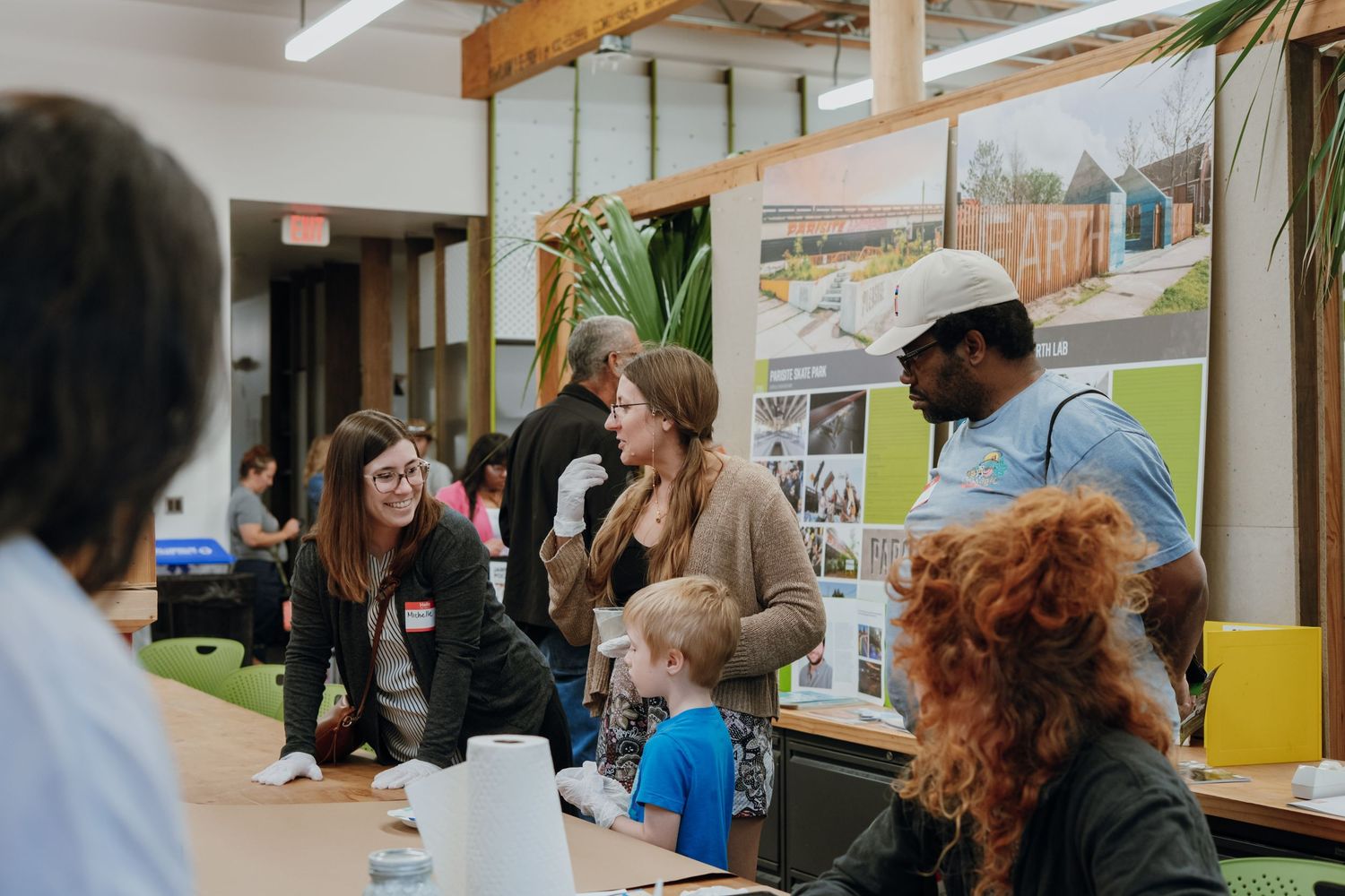 People gather at an indoor community event reviewing architectural design boards displayed on a table.