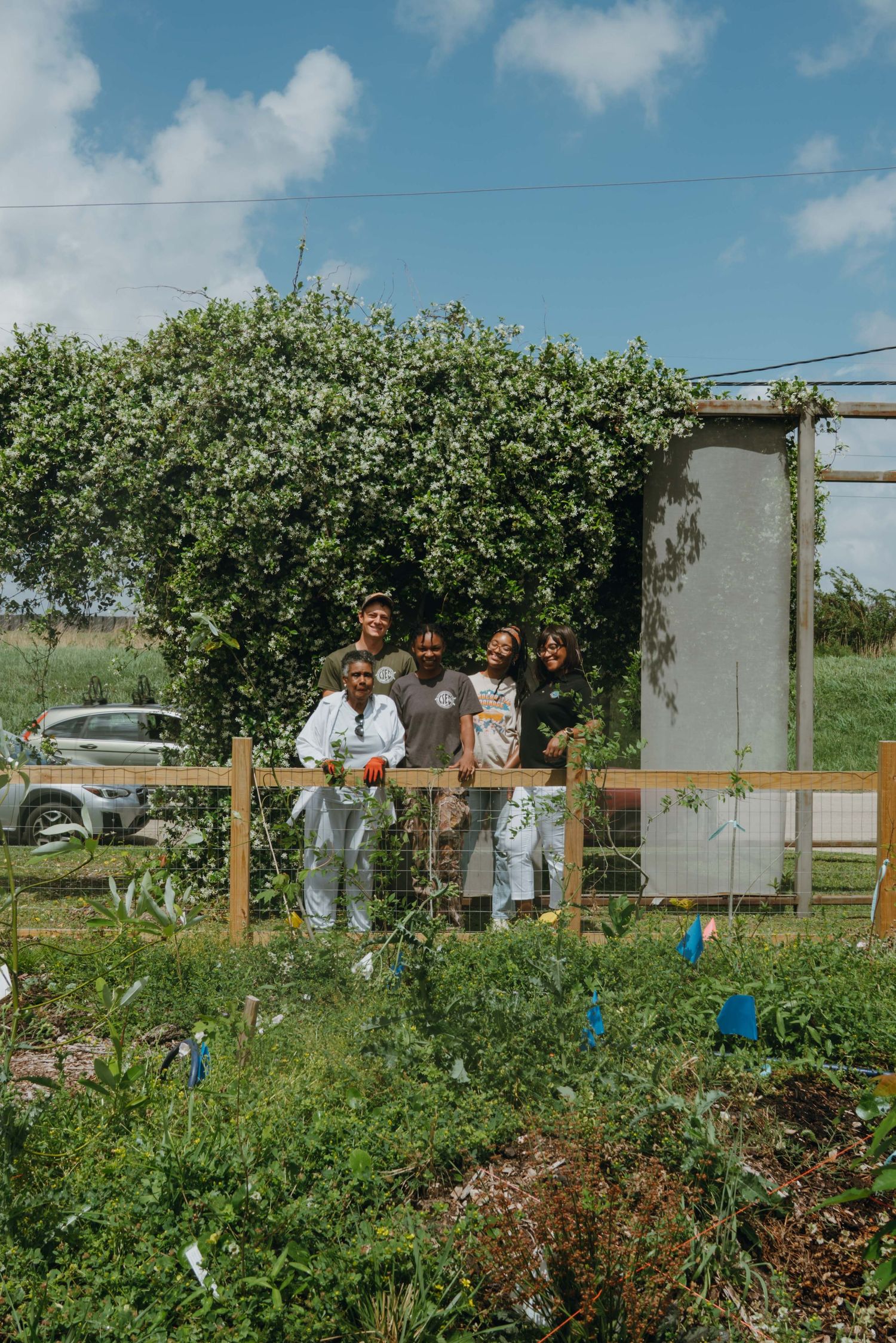 Group of four people pose together in lush community garden space.