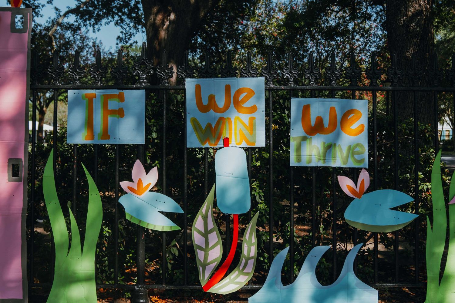 Colorful IF WE WIN WE LIVE signs displayed on a fence with painted flower decorations.