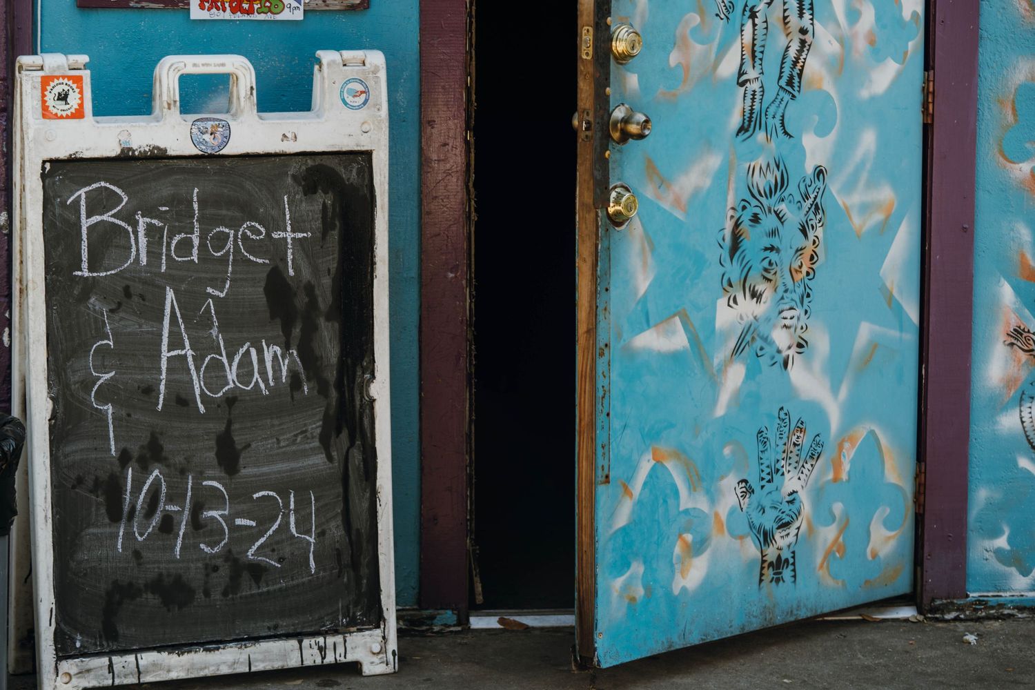 Chalkboard sign reading Bridget and Adam 10-13-24 on colorful graffiti wall outside a venue.