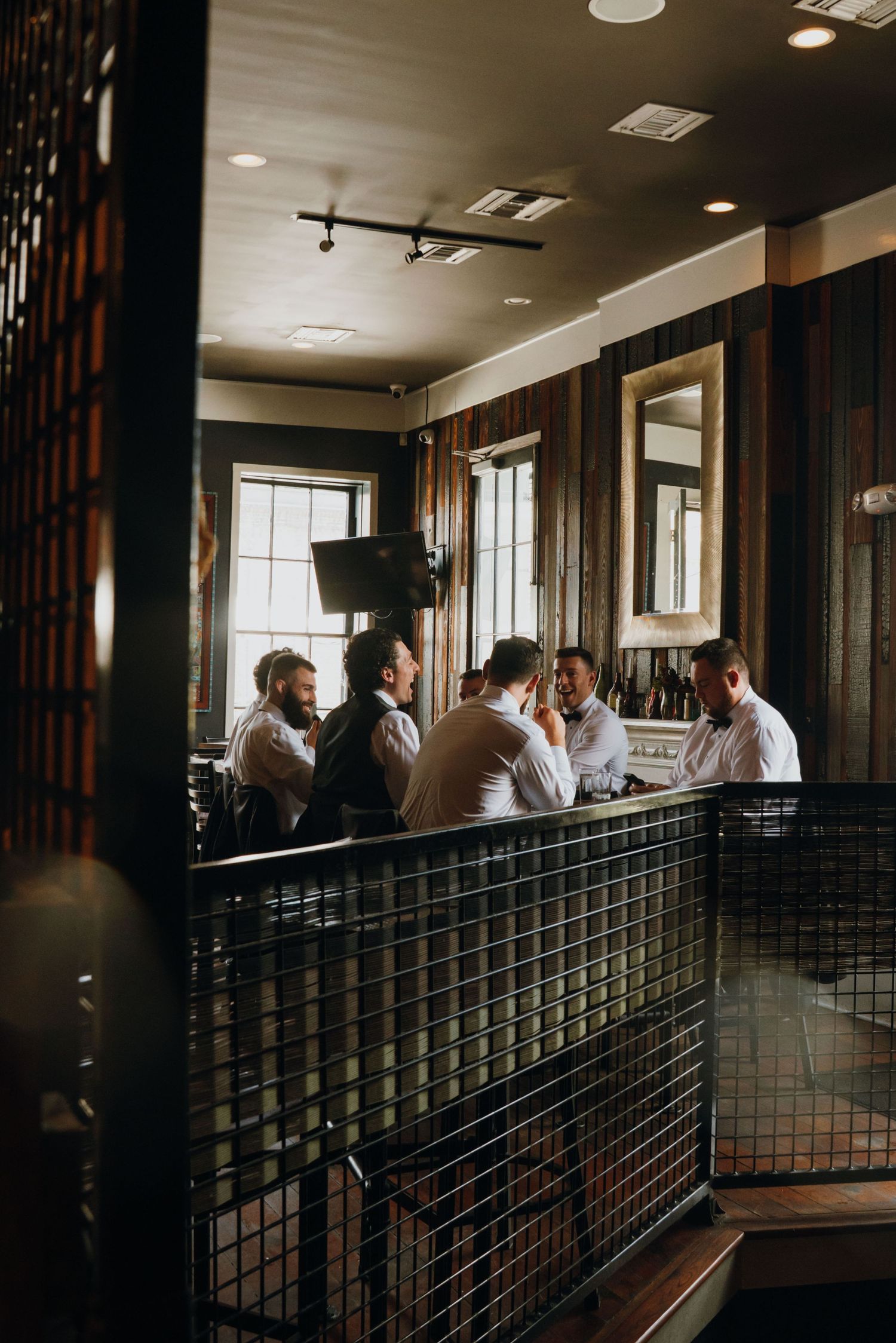 Groomsmen gathered at a rustic bar in white dress shirts before a wedding celebration.