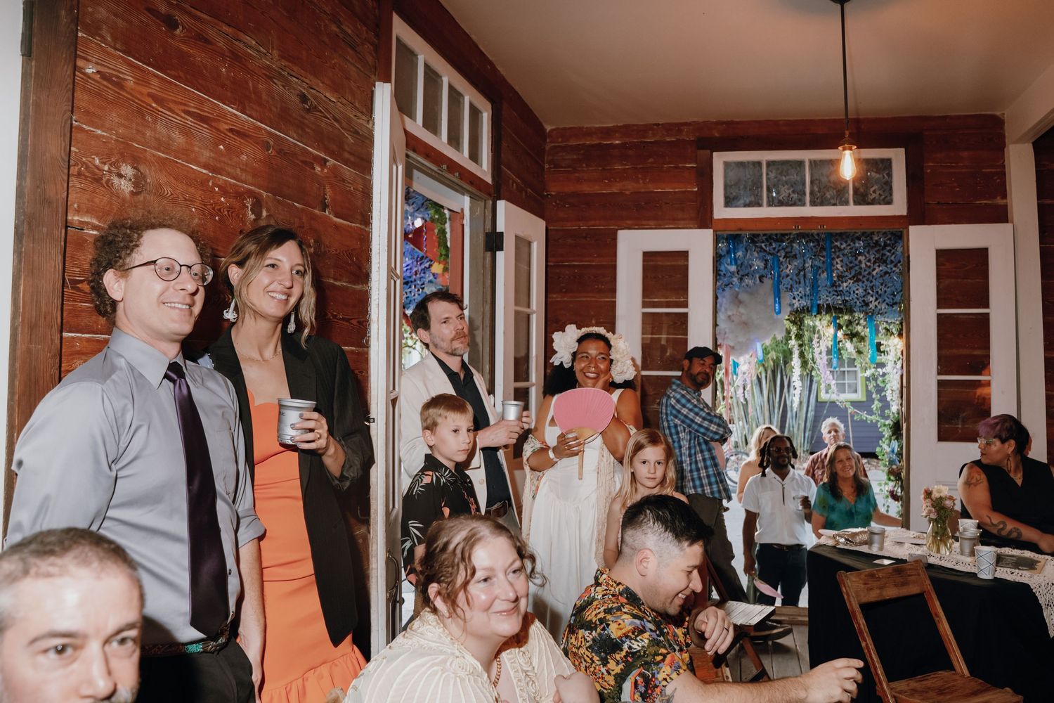 Wedding guests gather and mingle inside a warm, rustic wood-paneled reception venue.