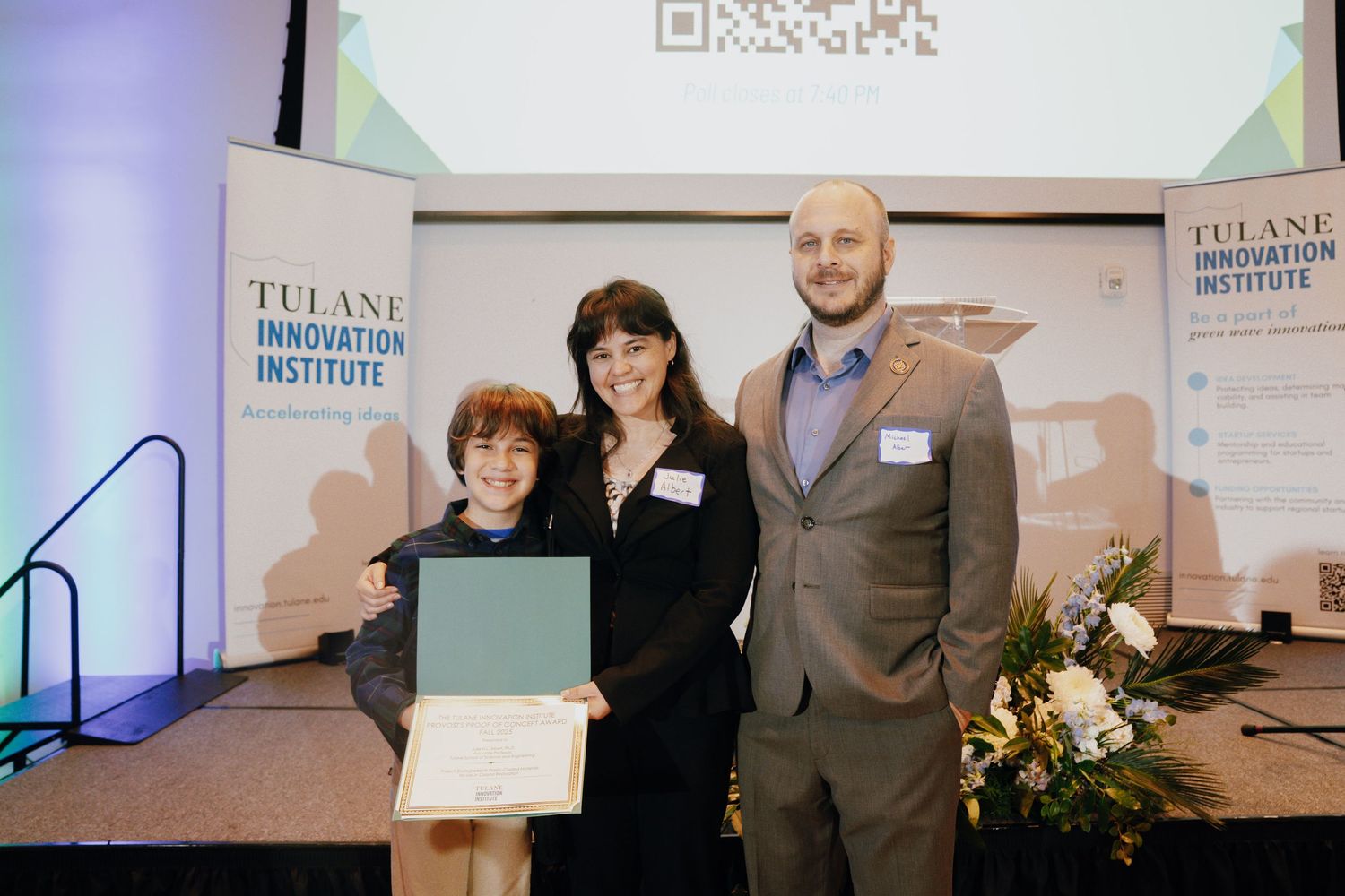 Three people pose with an award certificate at Tulane Innovation Institute recognition ceremony on stage.