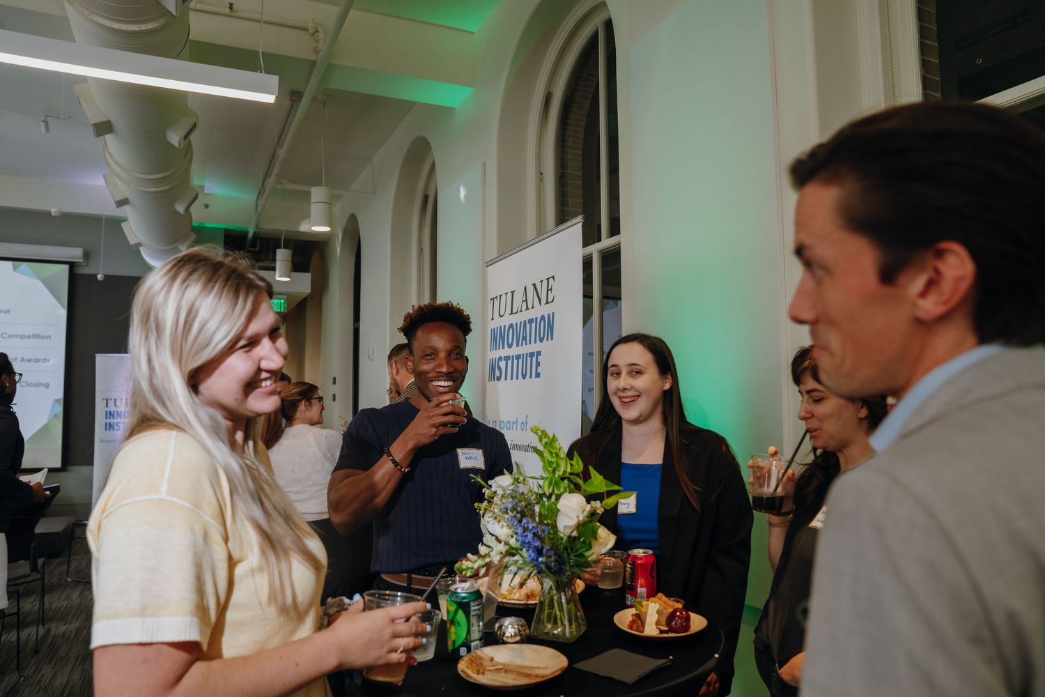 Professionals networking and socializing at Tulane Innovation Institute event with floral centerpiece.