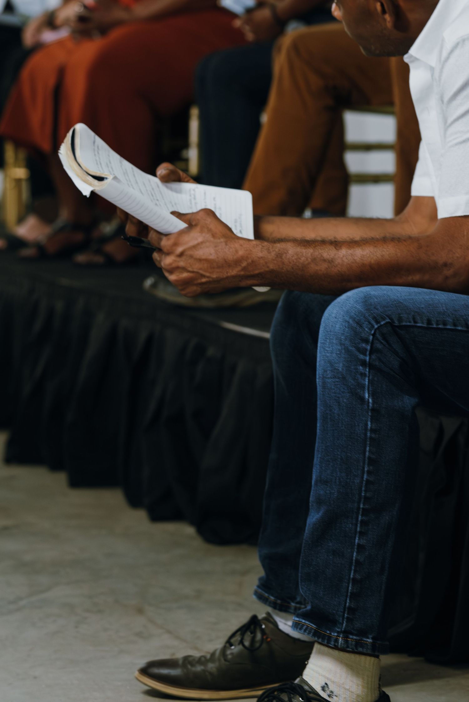 A man in jeans and white shirt reads printed documents while seated at a panel discussion event.