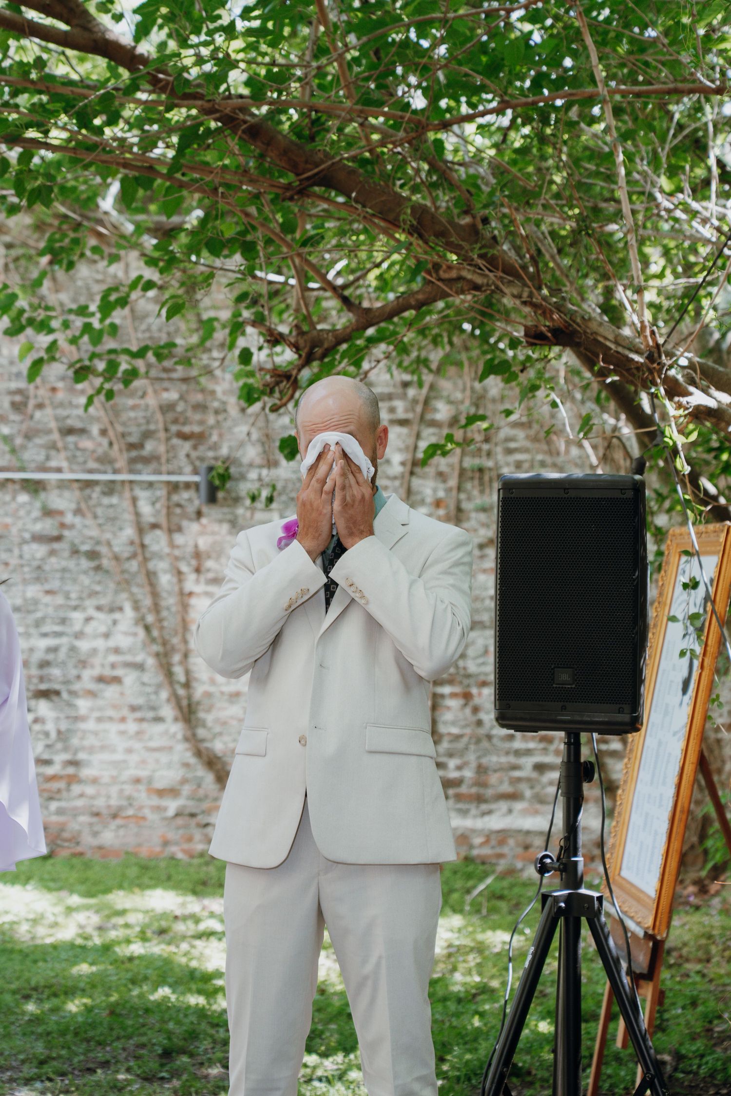 Emotional groom covering his face with a handkerchief during an outdoor wedding ceremony.