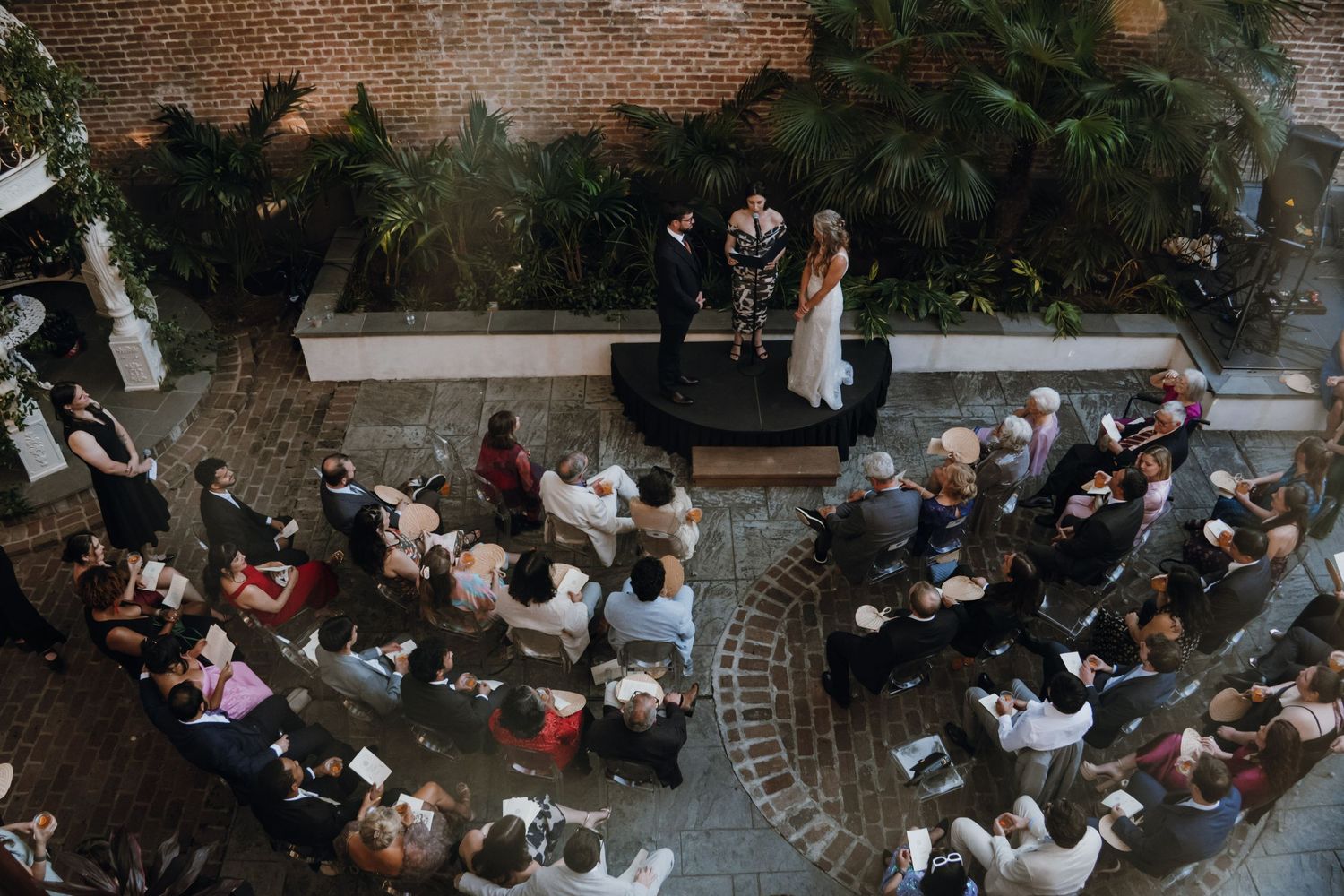 Aerial view of an intimate indoor wedding ceremony with guests seated on a brick courtyard.