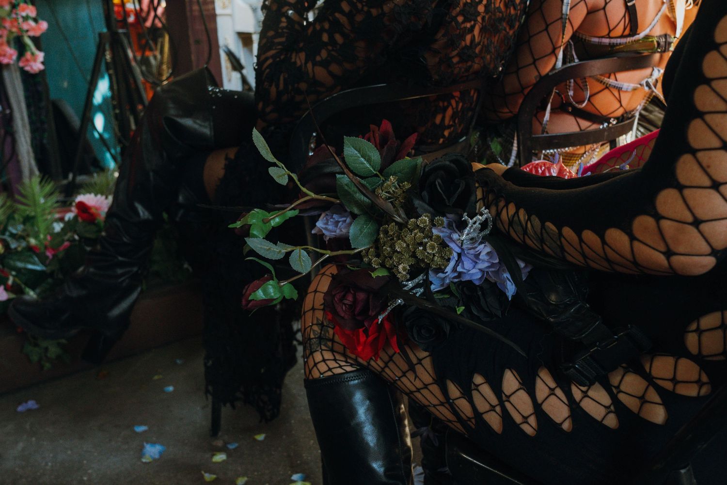 Close-up of a person in black fishnet stockings and boots holding a dark floral bouquet.