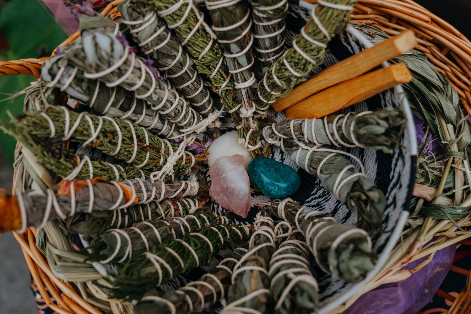 A wicker basket filled with white sage smudge sticks, cinnamon sticks, and healing crystals for spiritual cleansing.