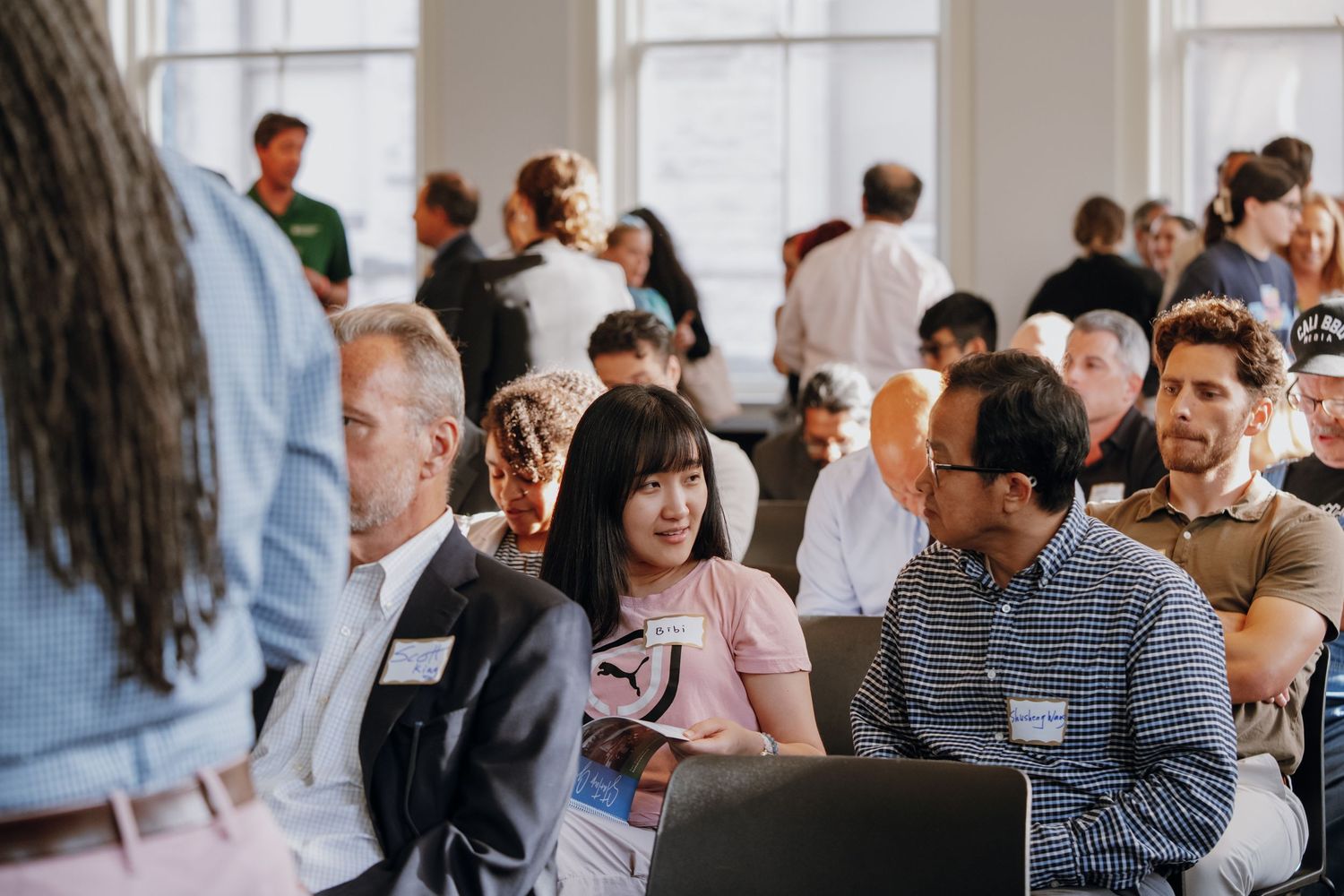 Group of professionals engaged in conversation at a bright, sunlit indoor conference event.