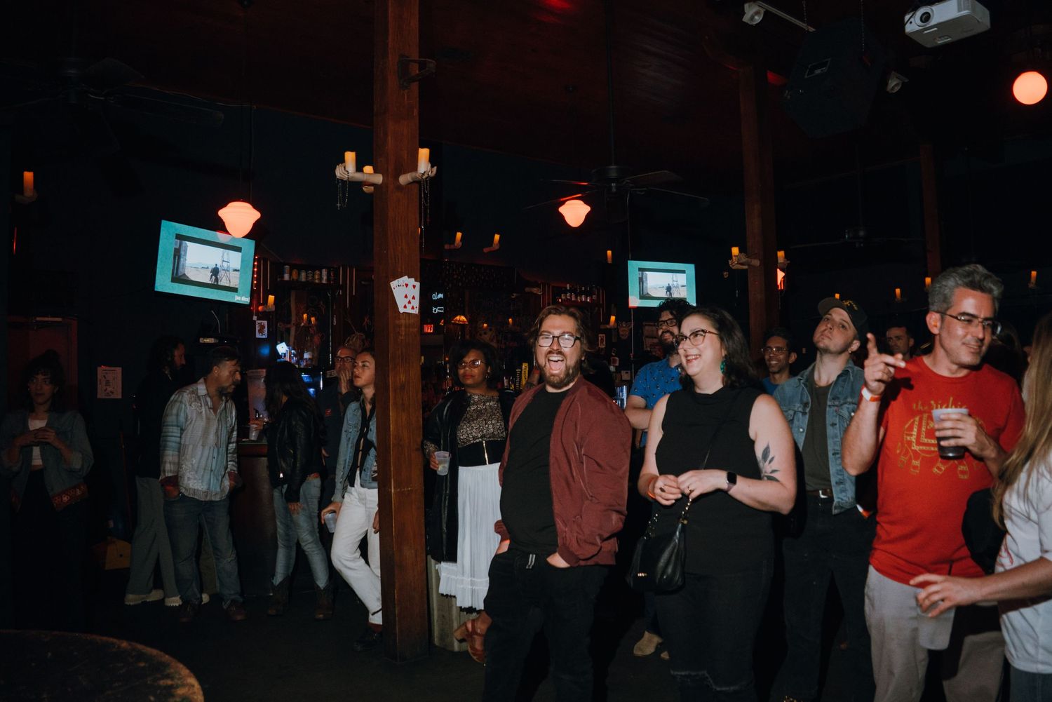 A diverse crowd of people gathered inside a dimly lit bar venue watching a live performance.