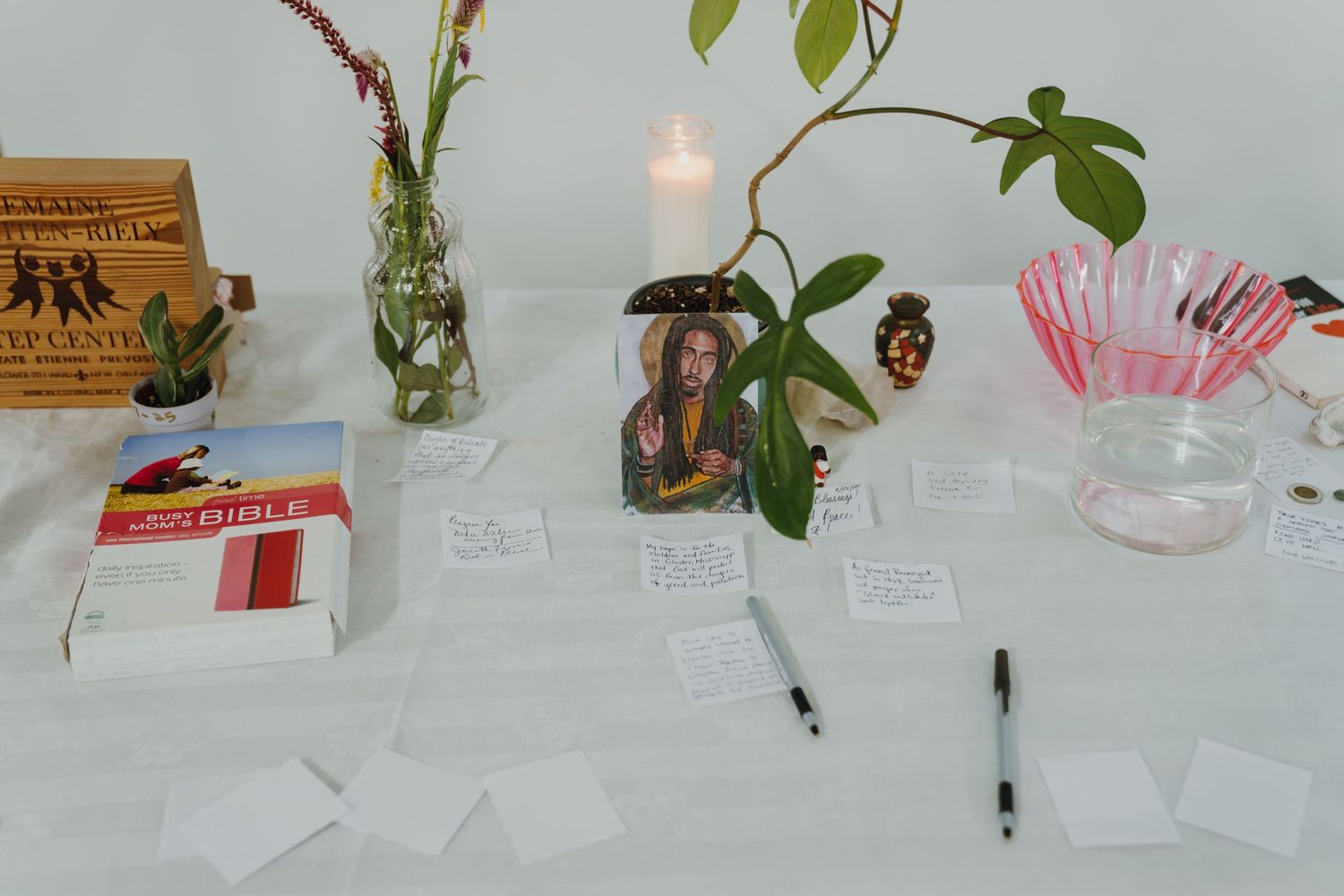 Community altar table with notes, candles, plants, books and photo of activist at event.