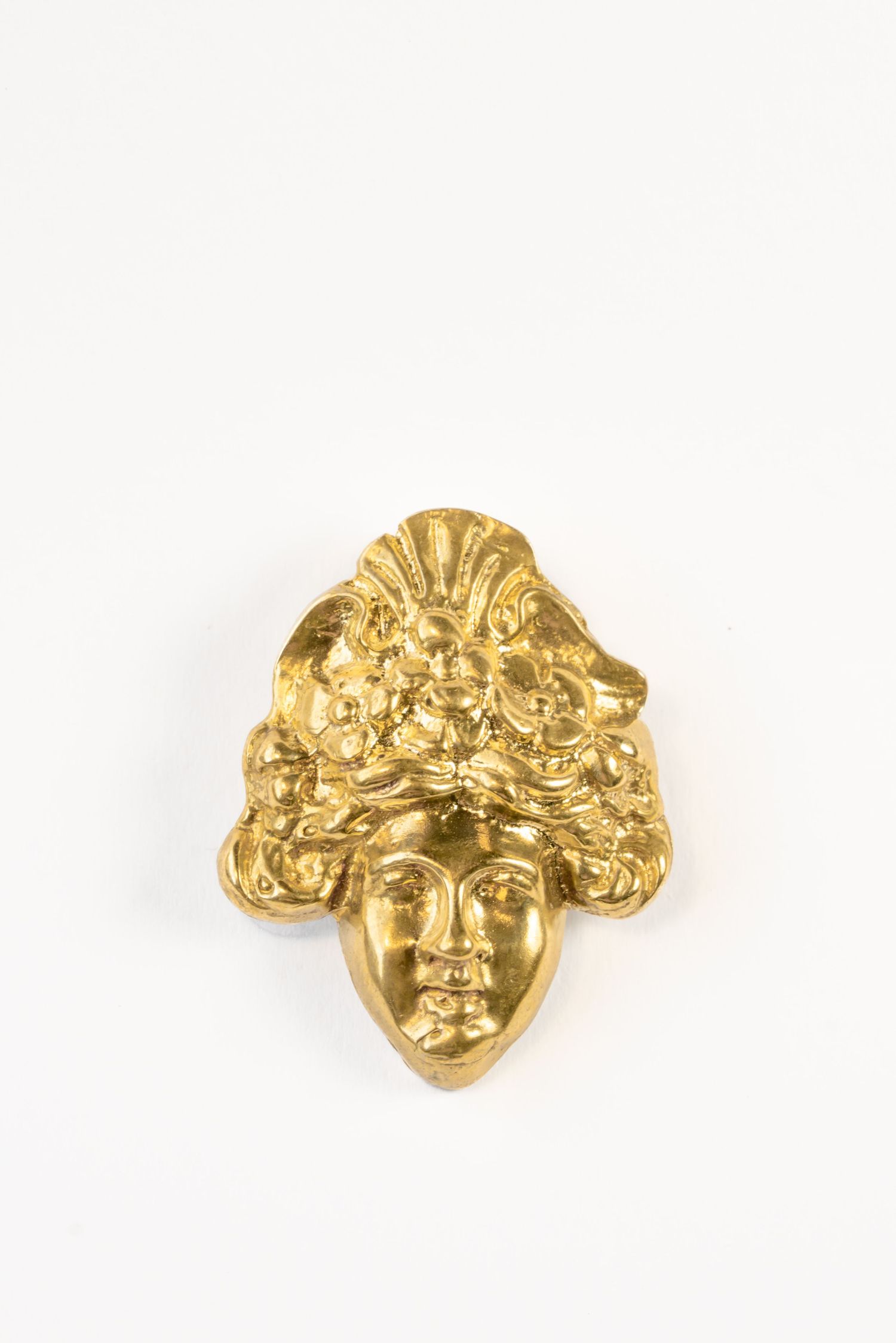 Ornate gold-plated face brooch with decorative floral headdress on white background.