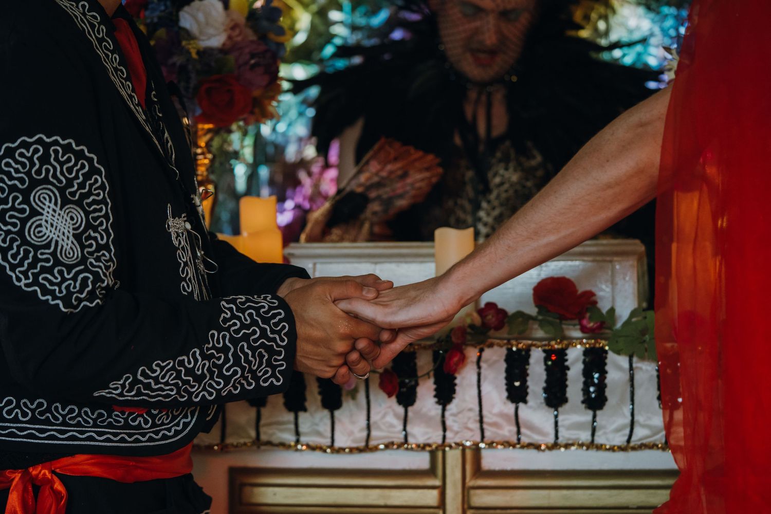 Two people in traditional Dia de los Muertos attire hold hands over a decorated piano with roses.