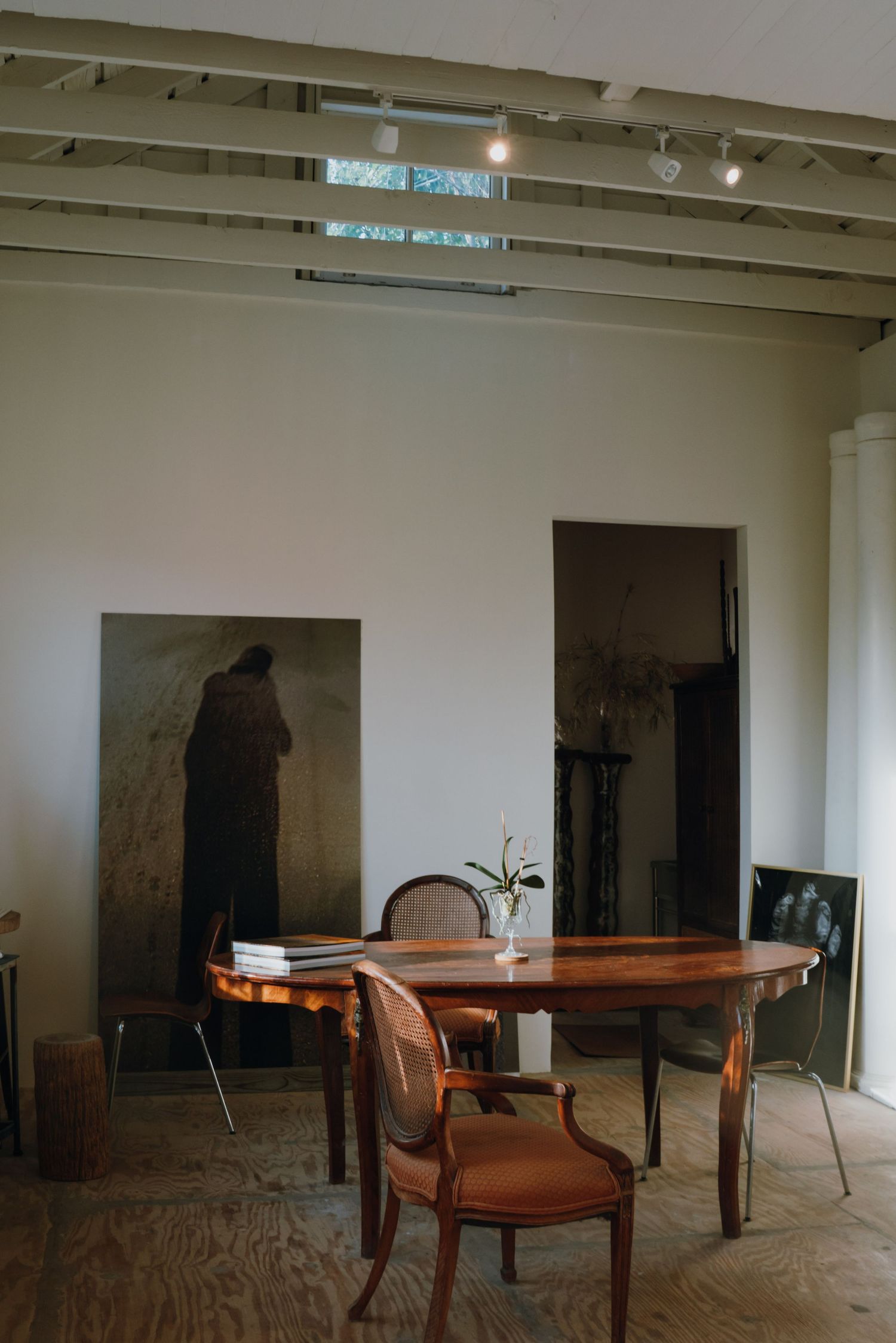 Elegant vintage room with oval wooden table, antique chair, and large figurative painting leaning on wall.