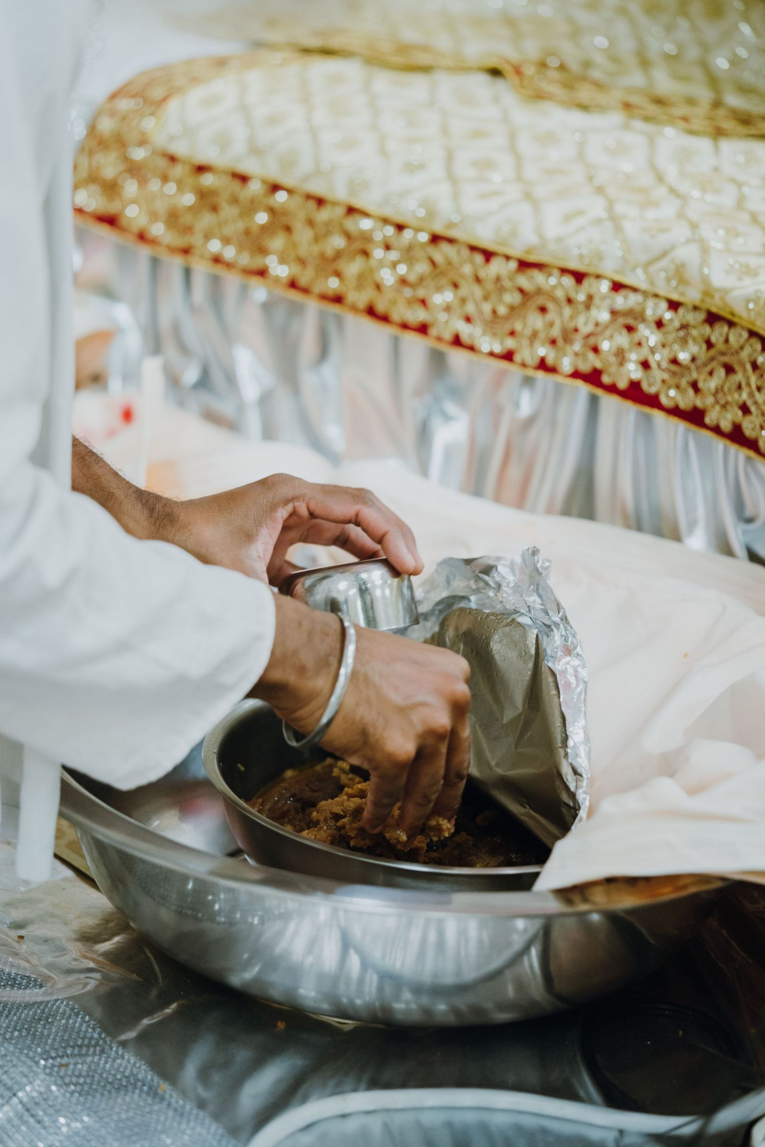 Hands preparing traditional Indian wedding ceremony offerings in a silver bowl with decorative fabric.