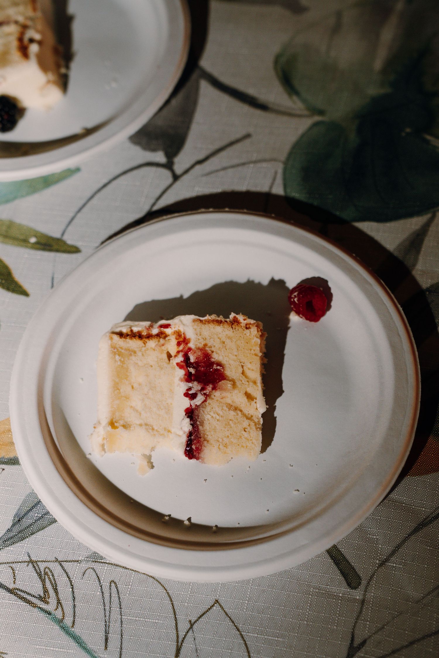Slice of white wedding cake with raspberry filling and fresh berry garnish on white plate.