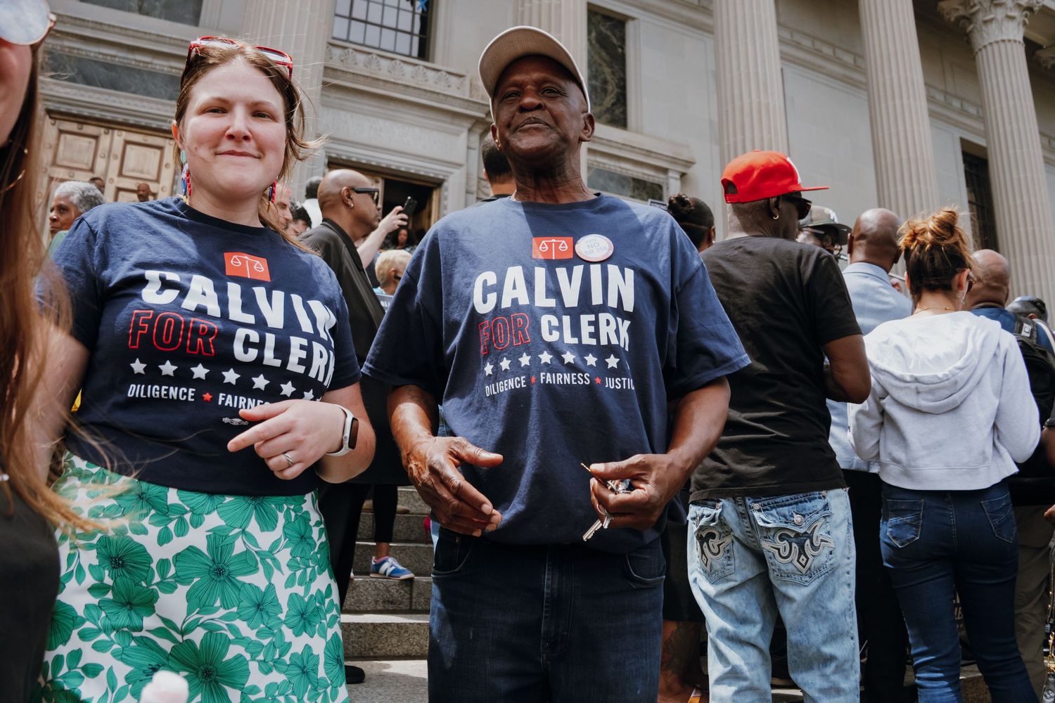 Two supporters wearing matching Calvin for Clerk campaign t-shirts posing together at a political rally.