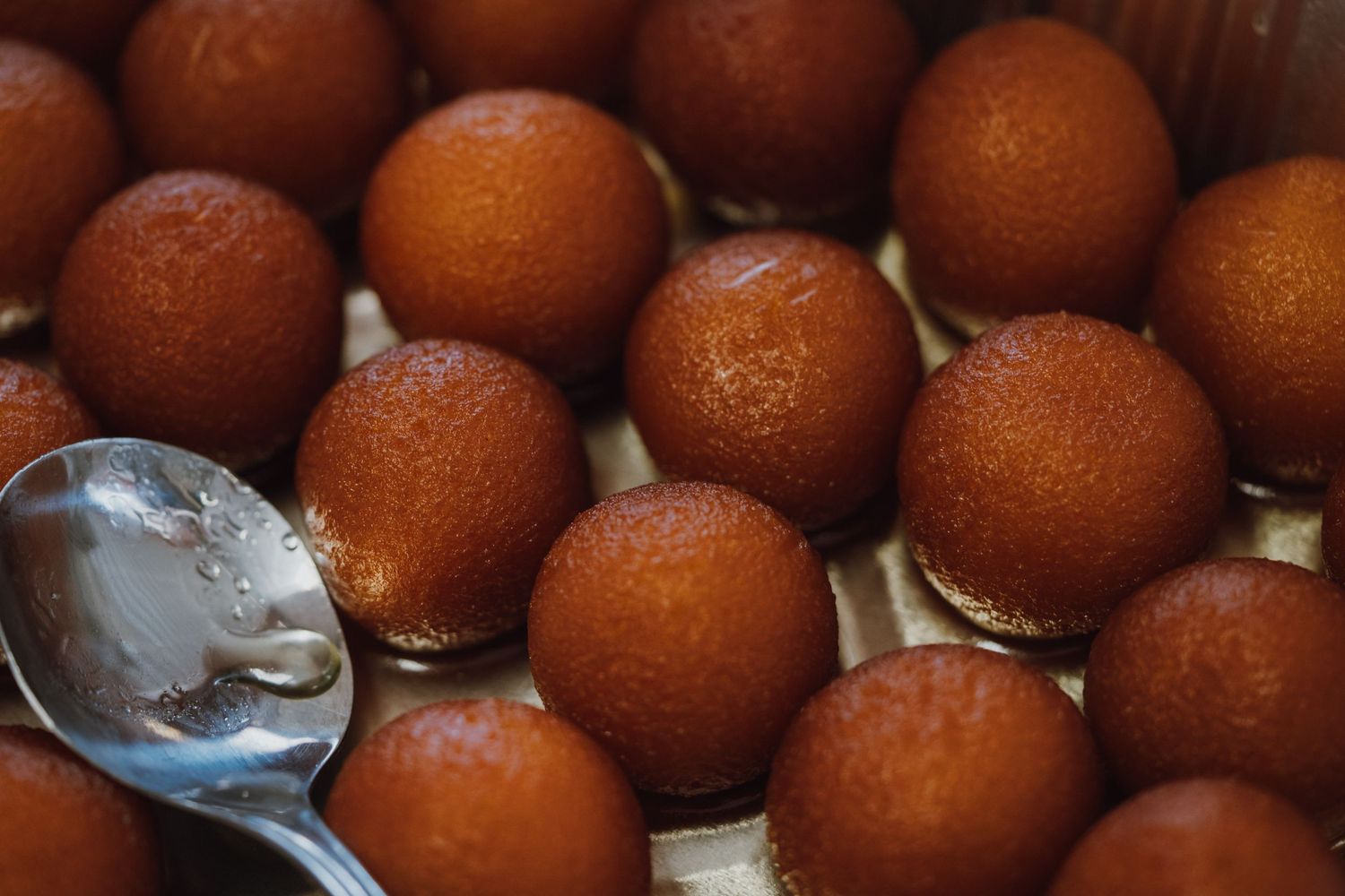 Close-up of golden-brown gulab jamun Indian sweet dessert balls arranged with a silver spoon.