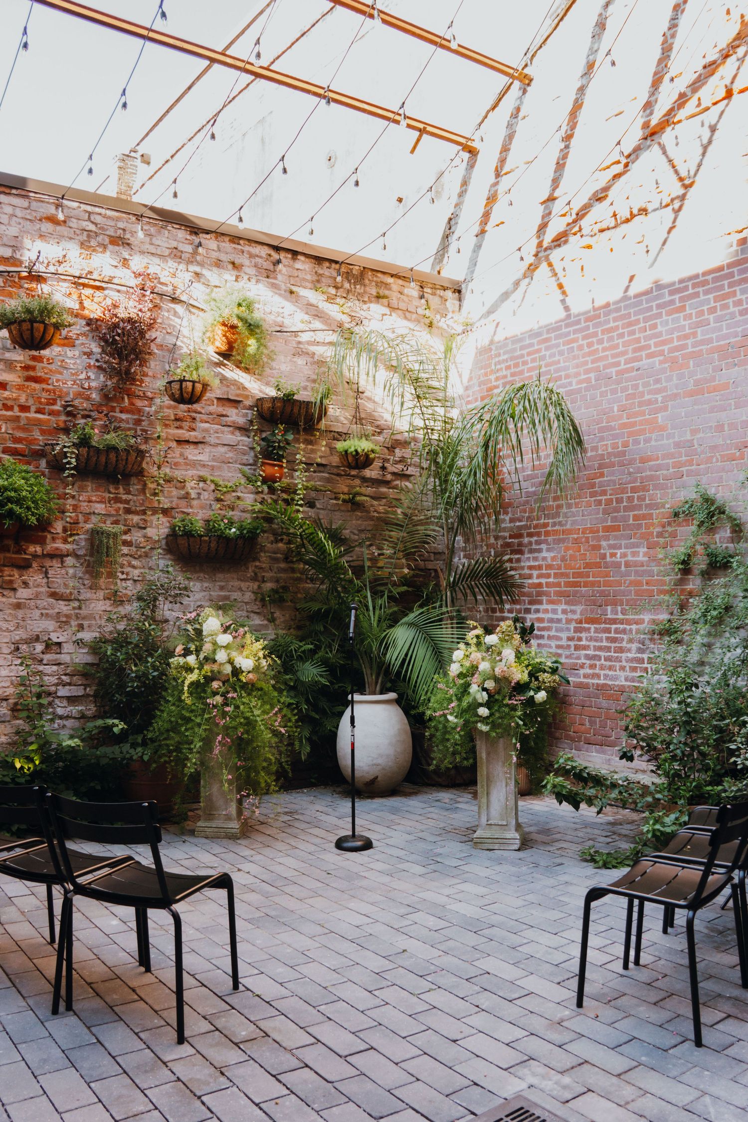 Intimate outdoor wedding ceremony courtyard with brick walls, string lights, tropical plants, and floral pedestals. New Orleans, Louisiana,