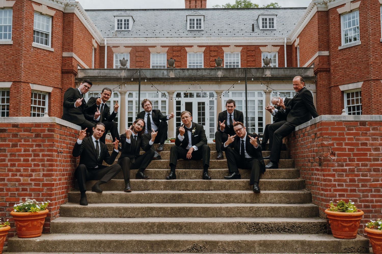 Groomsmen in black suits posing playfully on brick steps outside an elegant estate. New Orleans, Louisiana, Mississippi