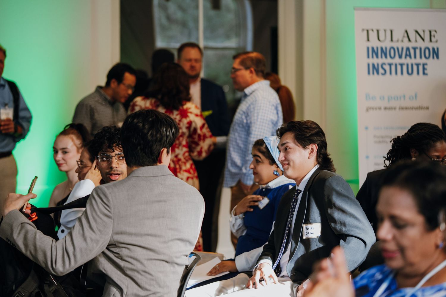 Professionals engaged in discussion at Tulane Innovation Institute networking event with green lighting.