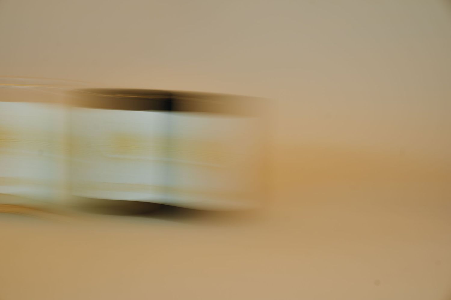 A motion-blurred vehicle captured in warm sandy tones creating an abstract speed effect.