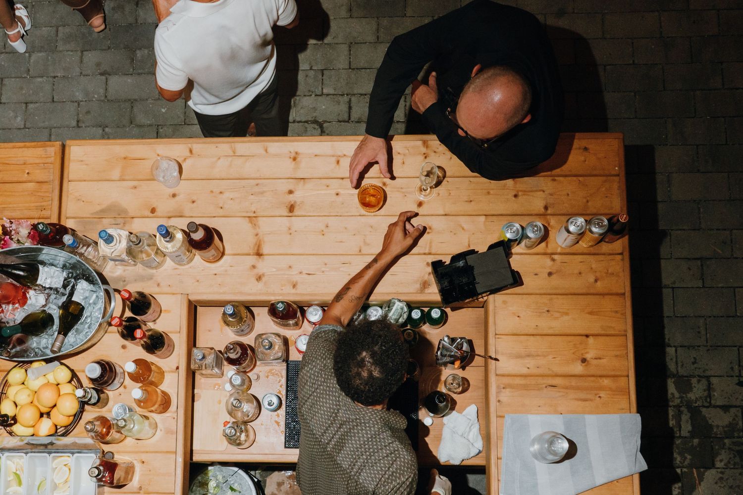 Aerial view of guests gathered around wooden table with drinks and food at casual outdoor wedding reception. New Orleans, Louisiana, Mississ
