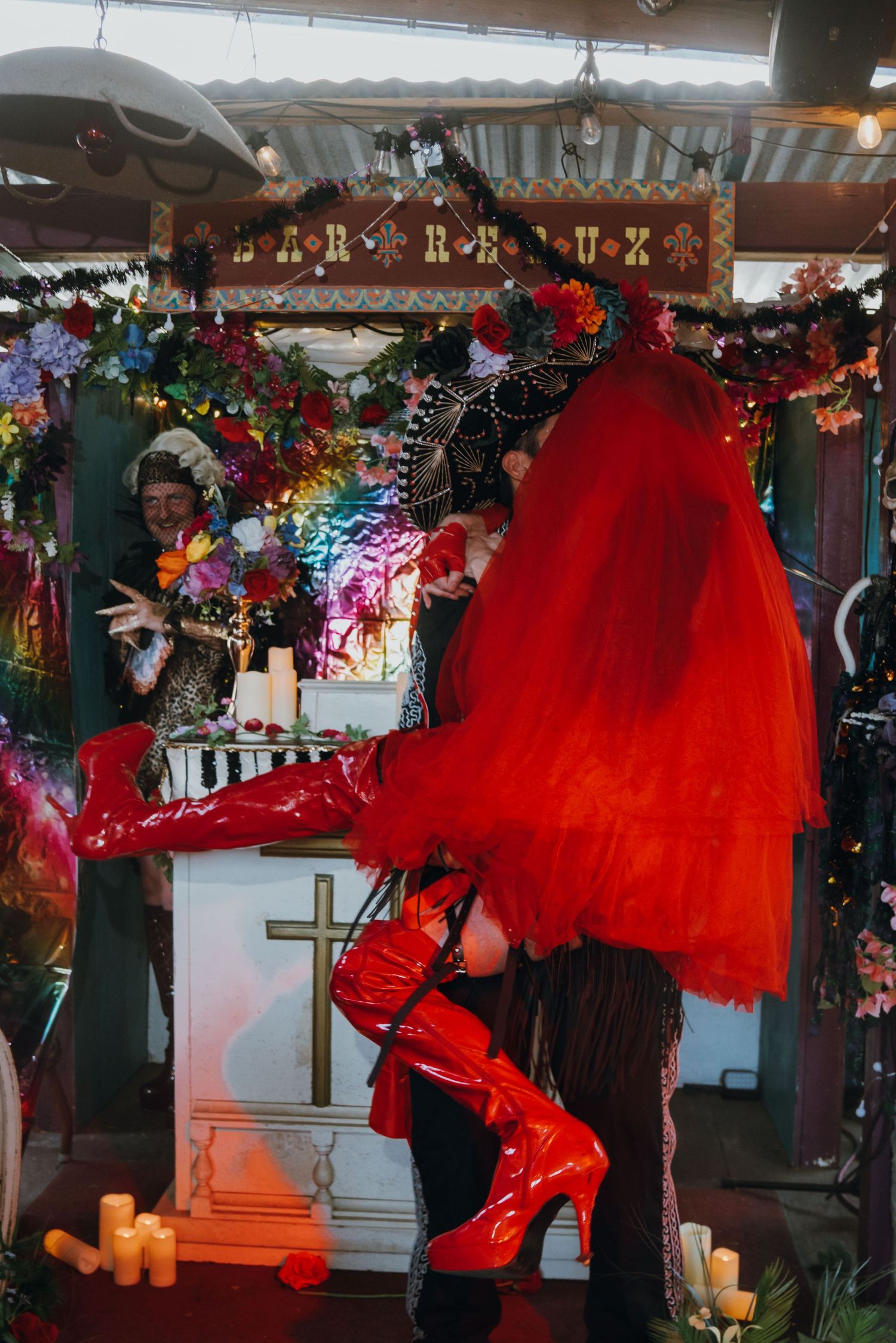 Person in dramatic red tulle skirt and red platform boots poses at a colorful decorated wedding altar.