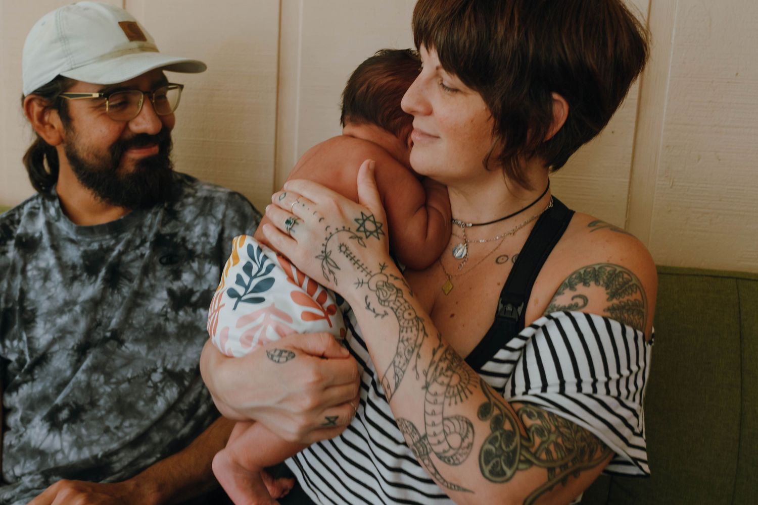 New parents with tattoos smiling and bonding with their newborn baby indoors. New Orleans, Louisiana, Mississippi