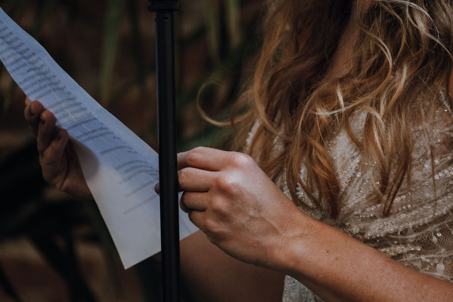 Close-up of bride holding wedding vow paper at an outdoor ceremony with bokeh background.