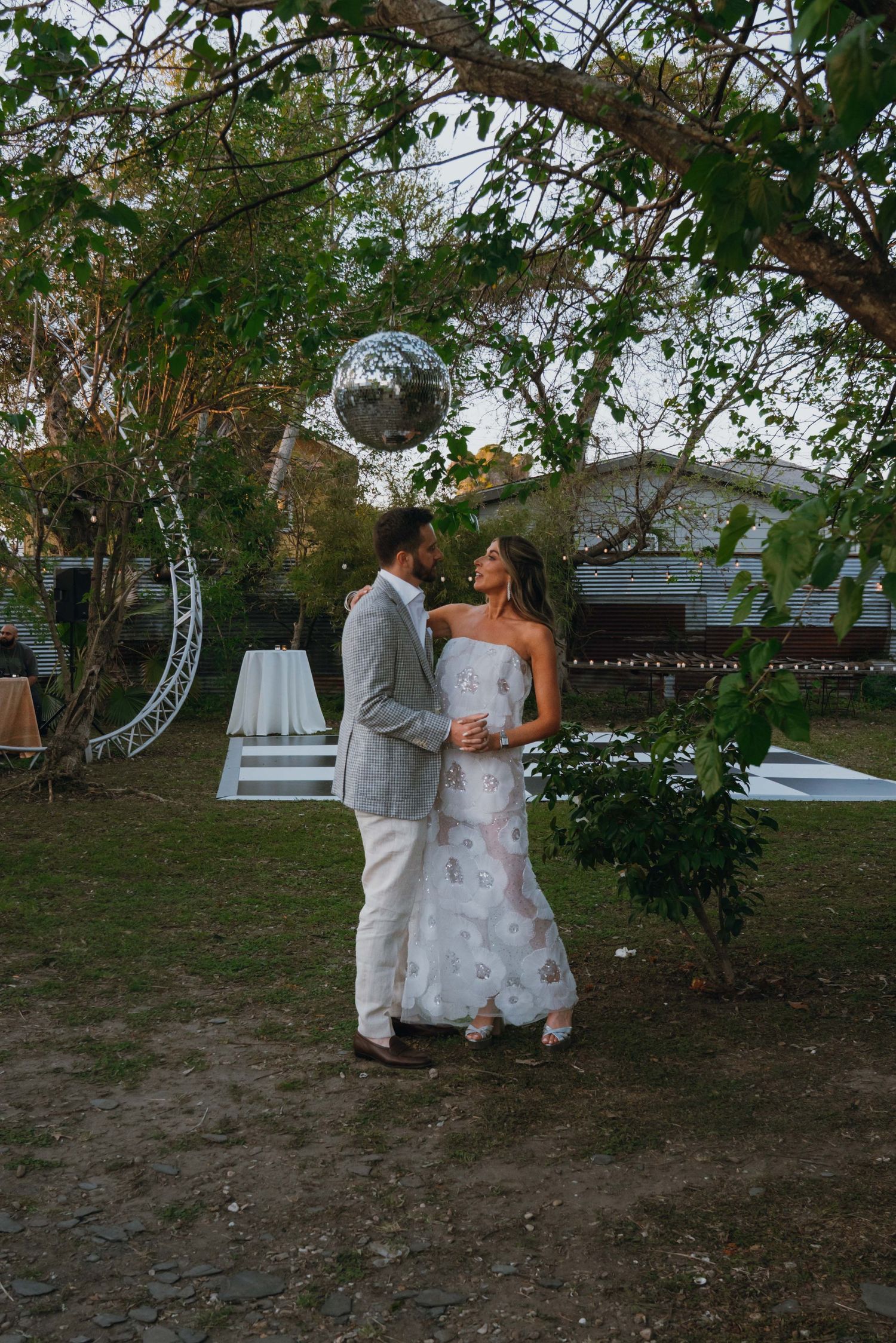 Bride and groom share romantic dance outdoors under disco ball and string lights at wedding reception.