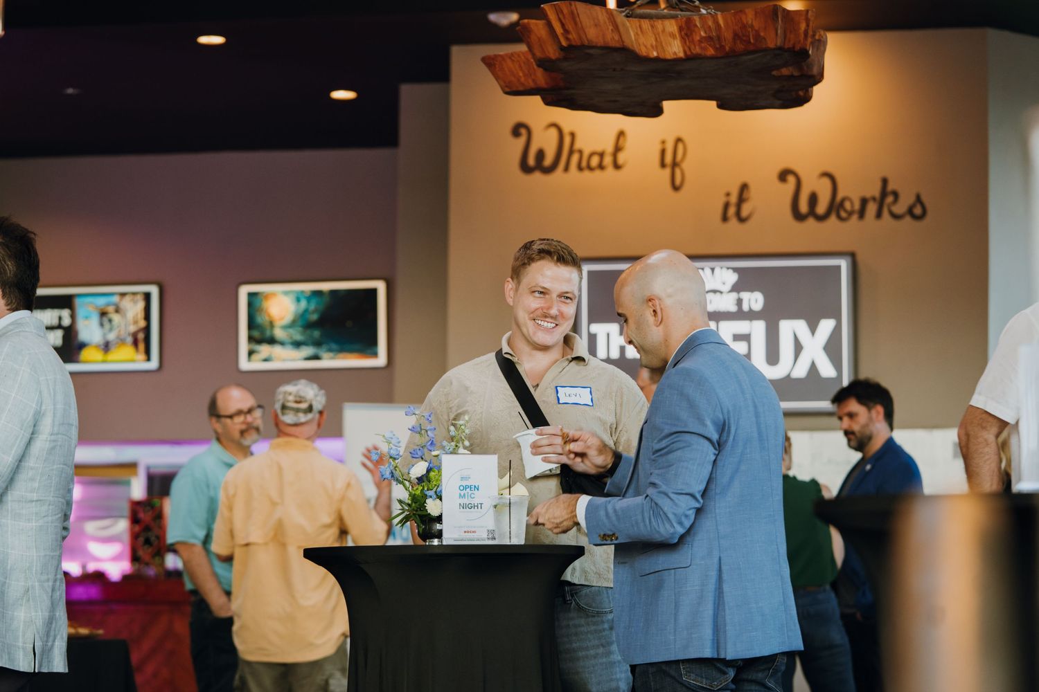 Two men networking at a business event inside a venue with a motivational quote on the wall.