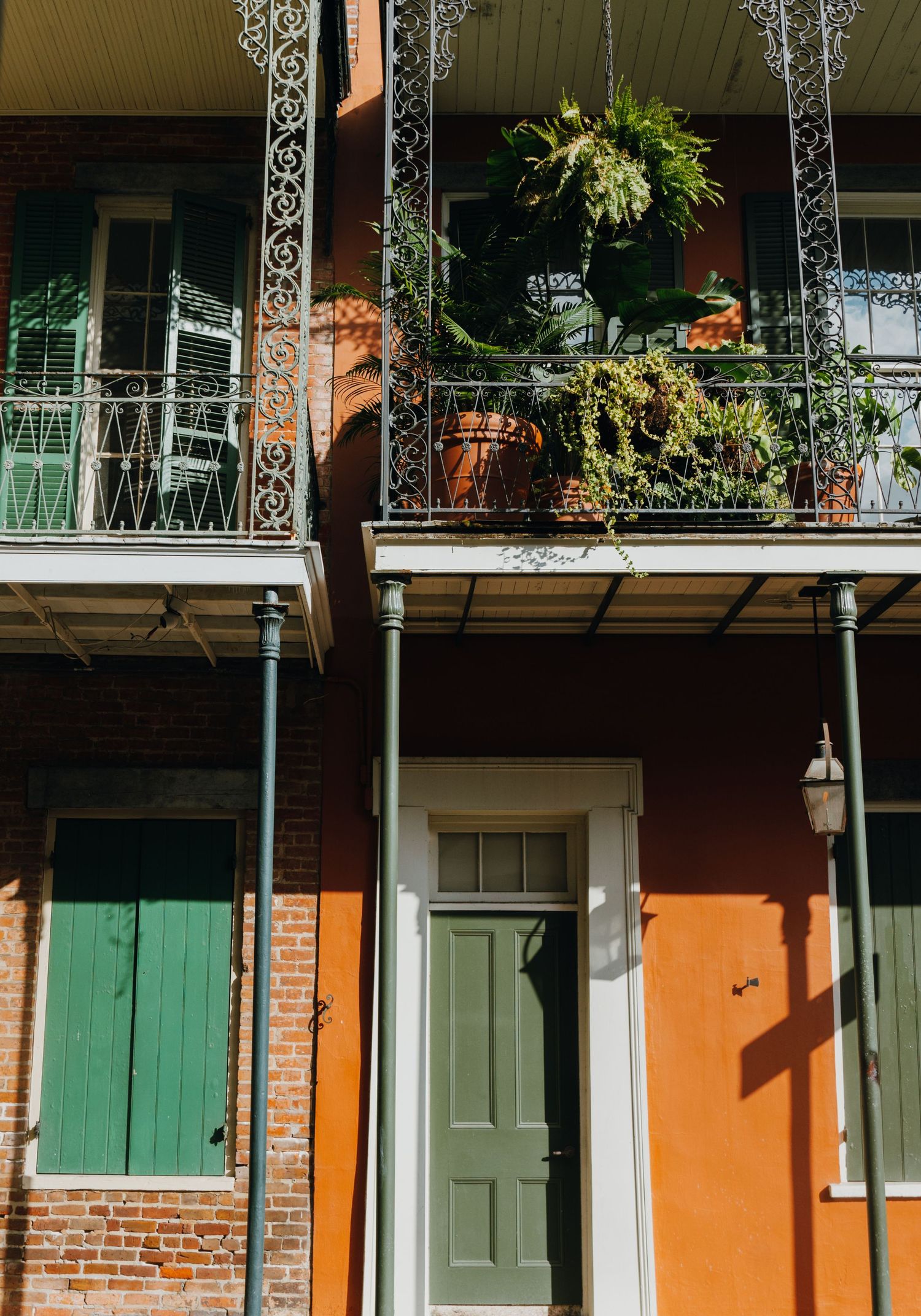 Colorful New Orleans French Quarter building with ornate iron balcony and hanging ferns.