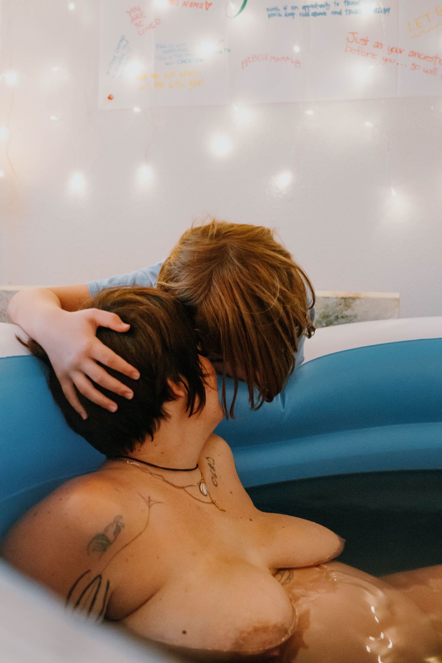 Child tenderly touches mothers head during home water birth labor in blue inflatable tub. New Orleans, Louisiana, Mississippi