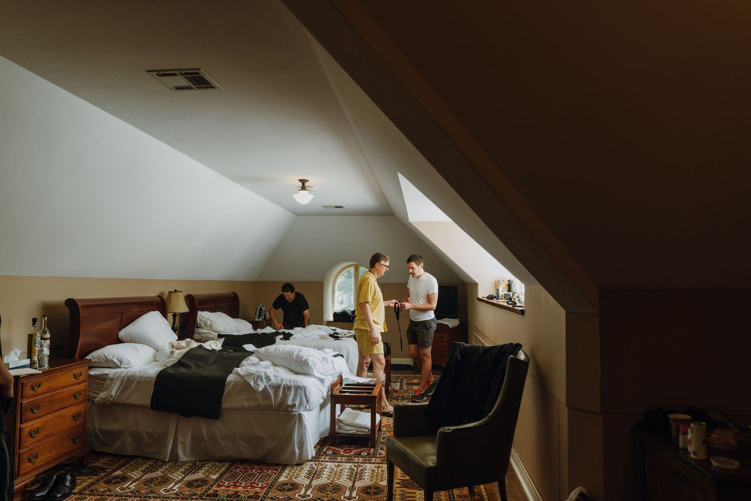 Groomsmen getting ready in a cozy attic bedroom with sloped ceilings and warm lighting. New Orleans, Louisiana, Mississippi